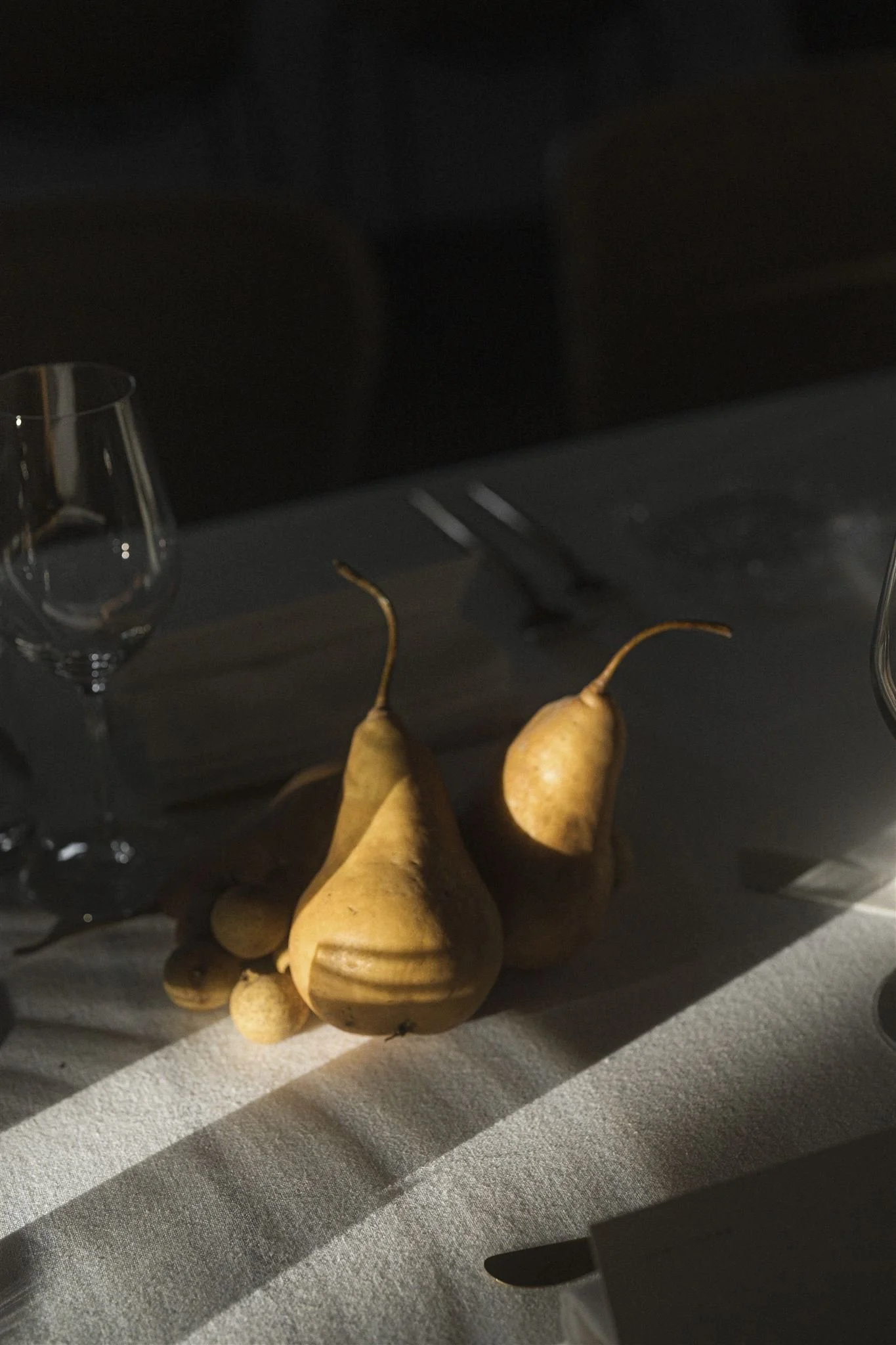 Three yellow pears on a table with a wine glass, a phone, and a knife, with a dark background.