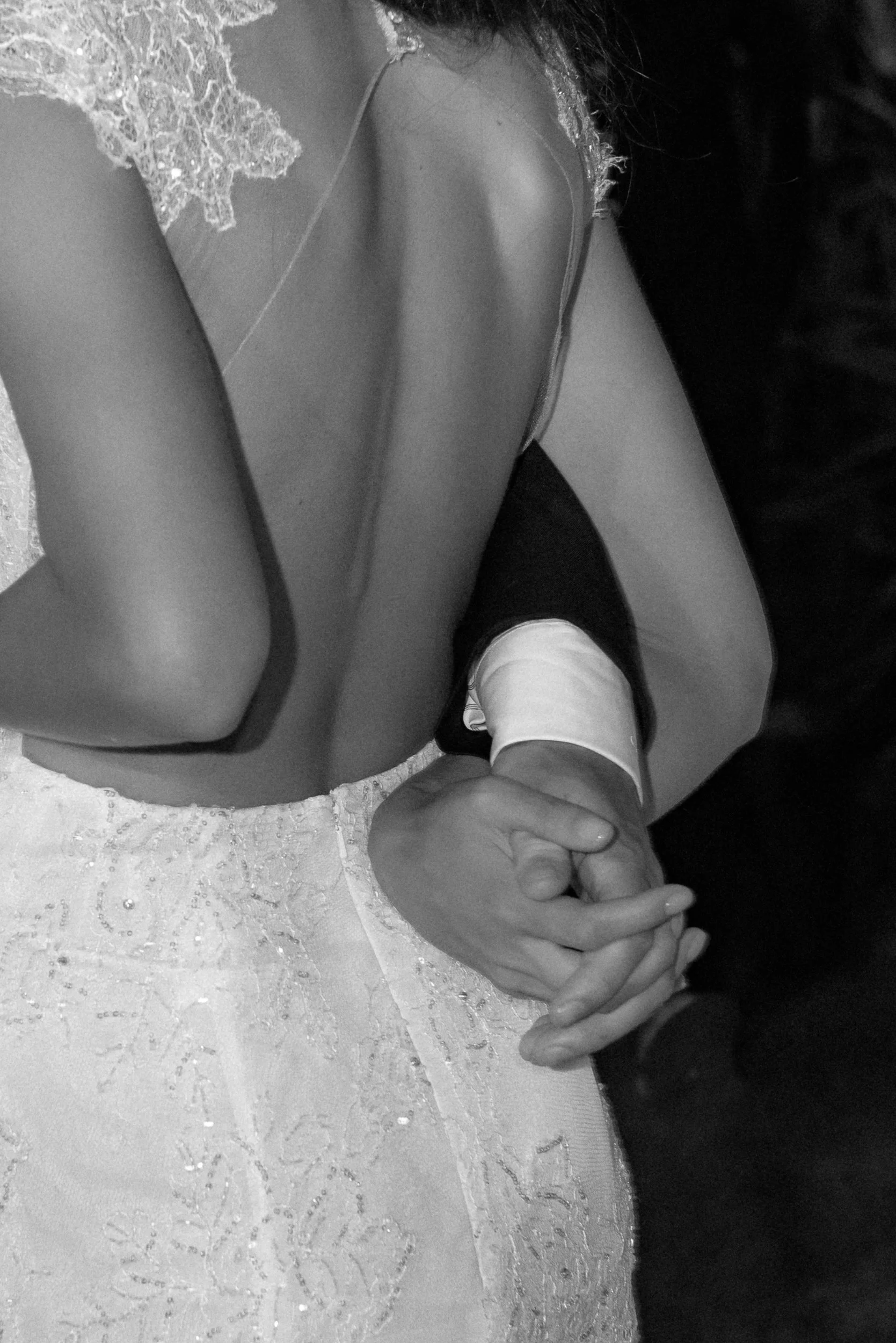 A young girl wearing a lace dress holding hands with a person in a dark suit. The girl is sitting on a lace tablecloth.