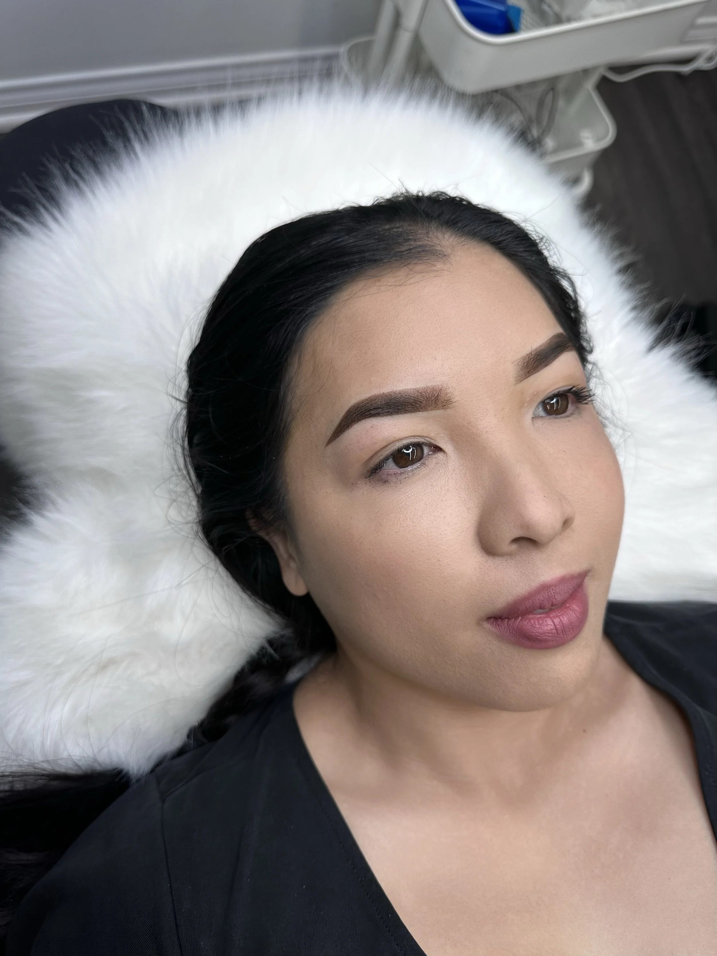 A woman with dark hair and makeup lying on a white furry surface, possibly in a medical or beauty setting.