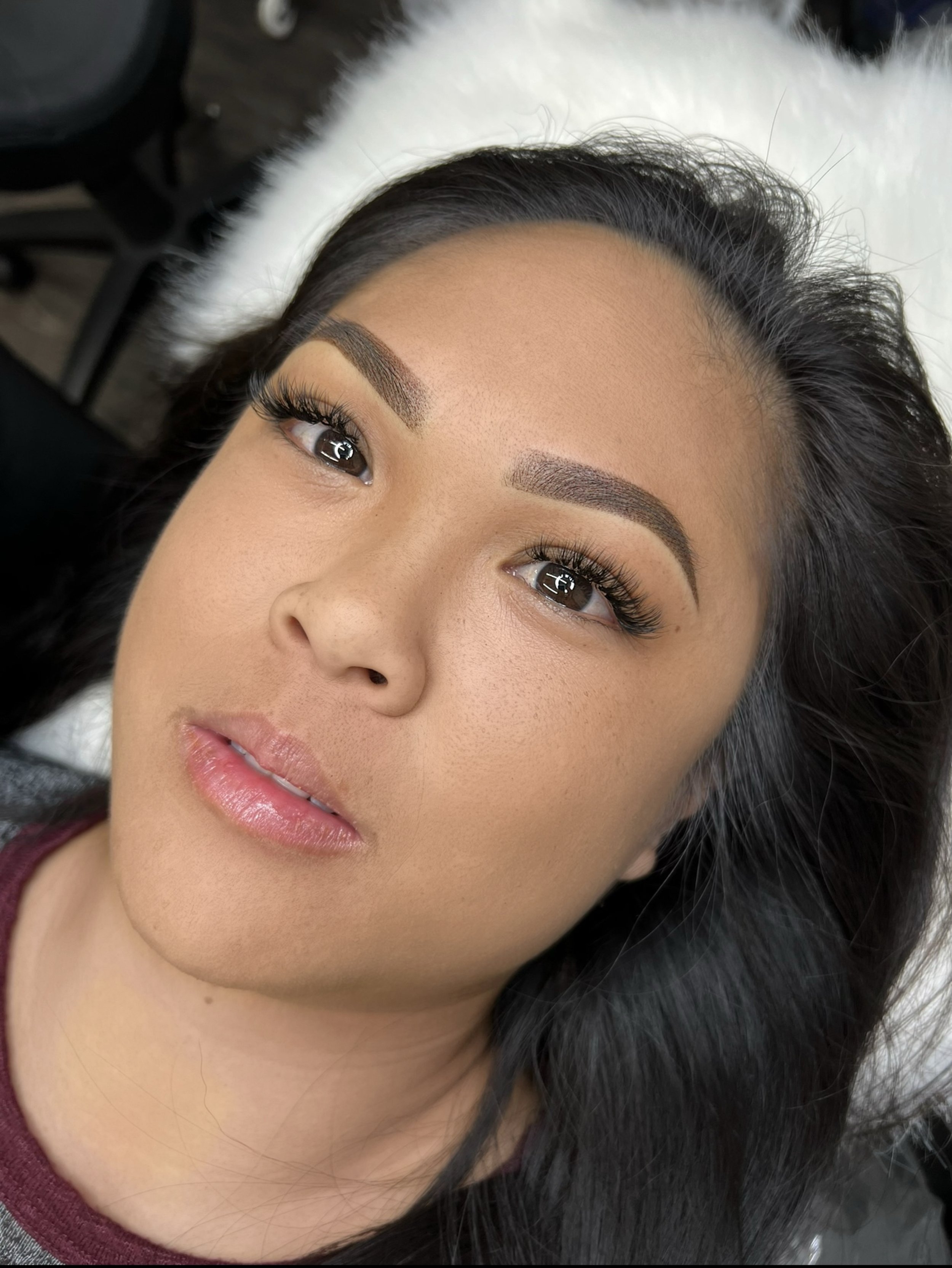 Close-up of a woman with dark hair, full eyebrows, and long eyelashes, lying down and looking upwards, with a soft expression.