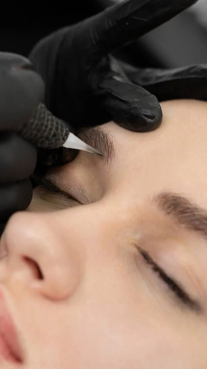 A person getting an eyebrow tattoo done by a professional artist wearing black gloves.