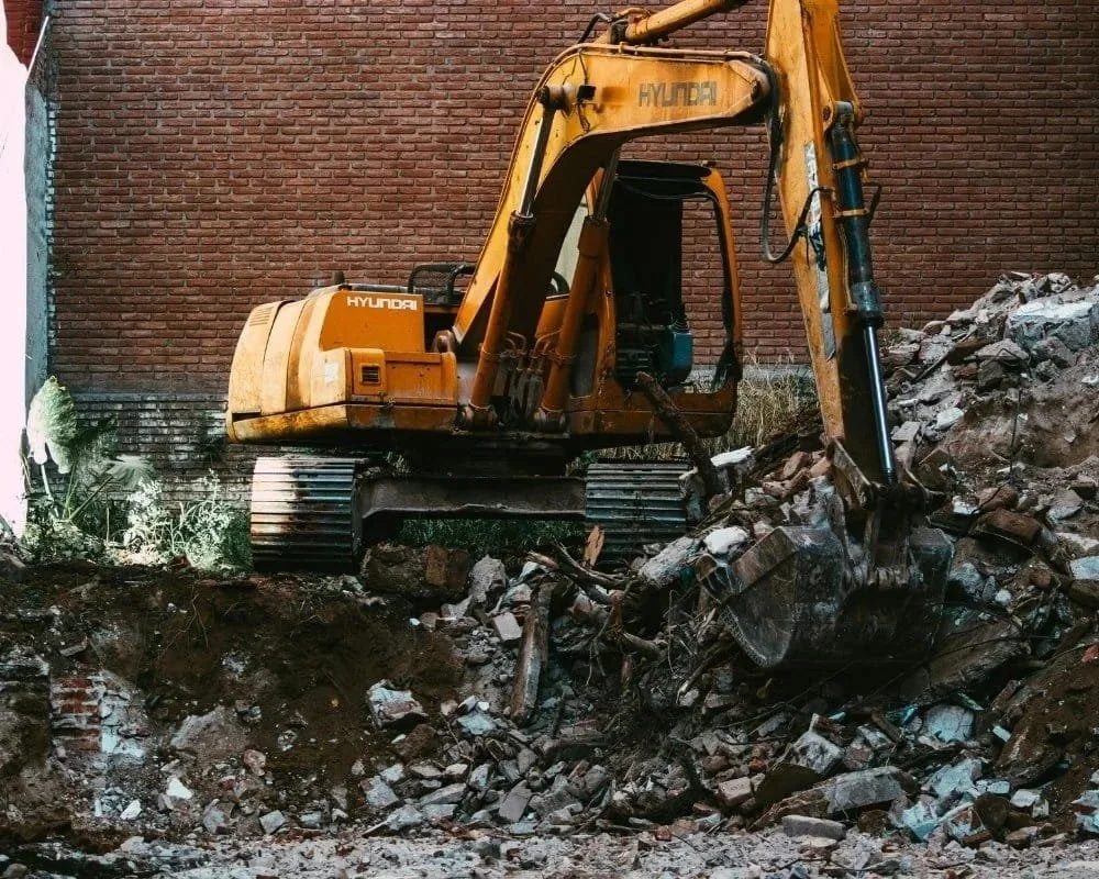 A yellow Hyundai excavator demolishing a brick building, with debris and rubble on the ground.