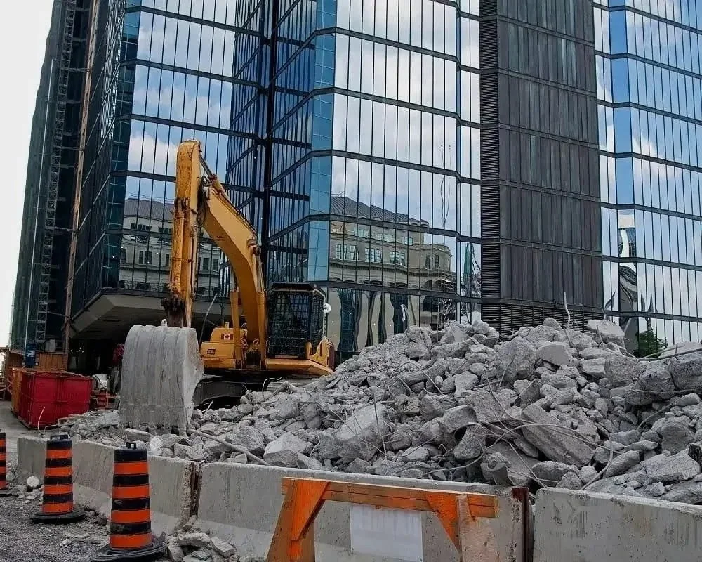 Construction site with a yellow excavator moving rubble in front of a modern glass building.