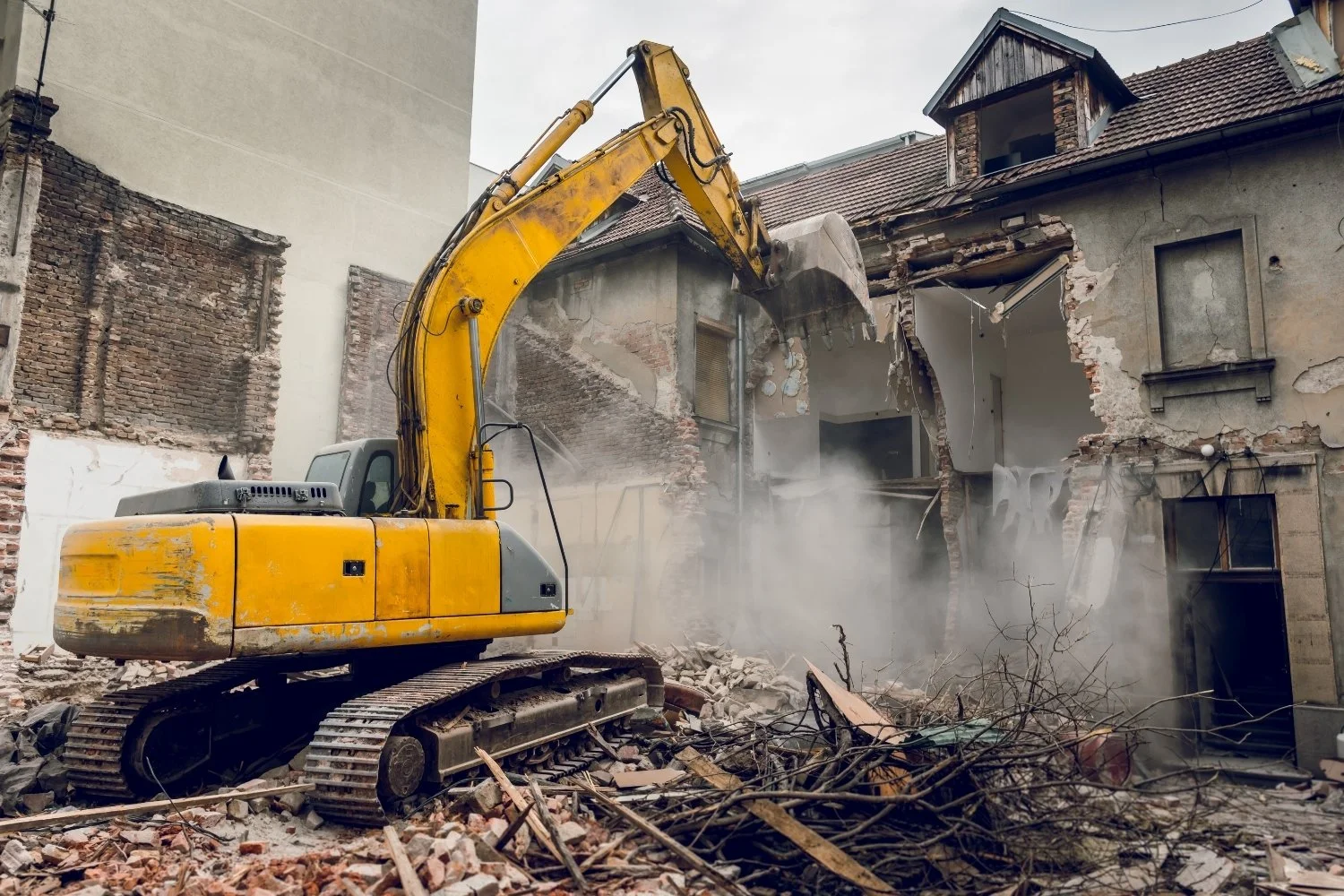 A yellow excavator demolishing a building, creating dust and debris.