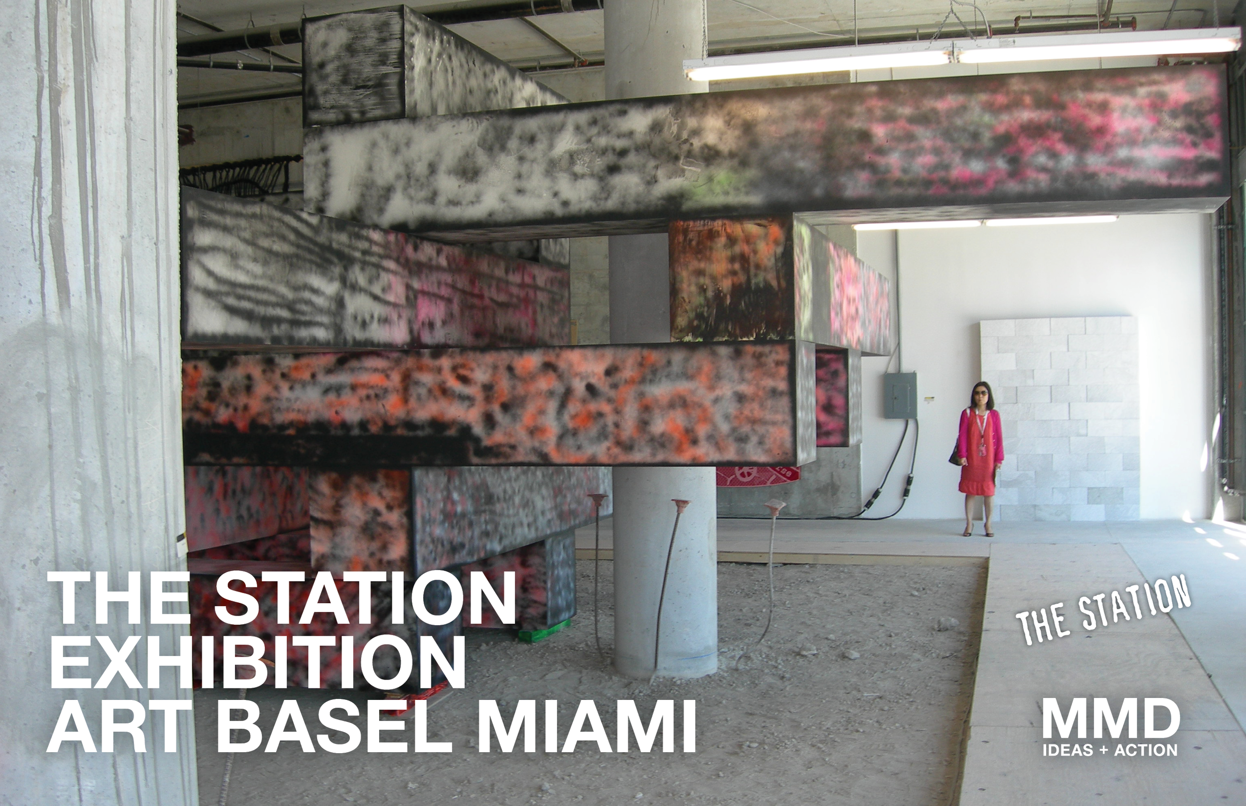 Art installation at The Station Exhibition, Art Basel Miami, featuring a suspended multicolored rectangular structure in an industrial space with a woman in pink dress standing in the background.
