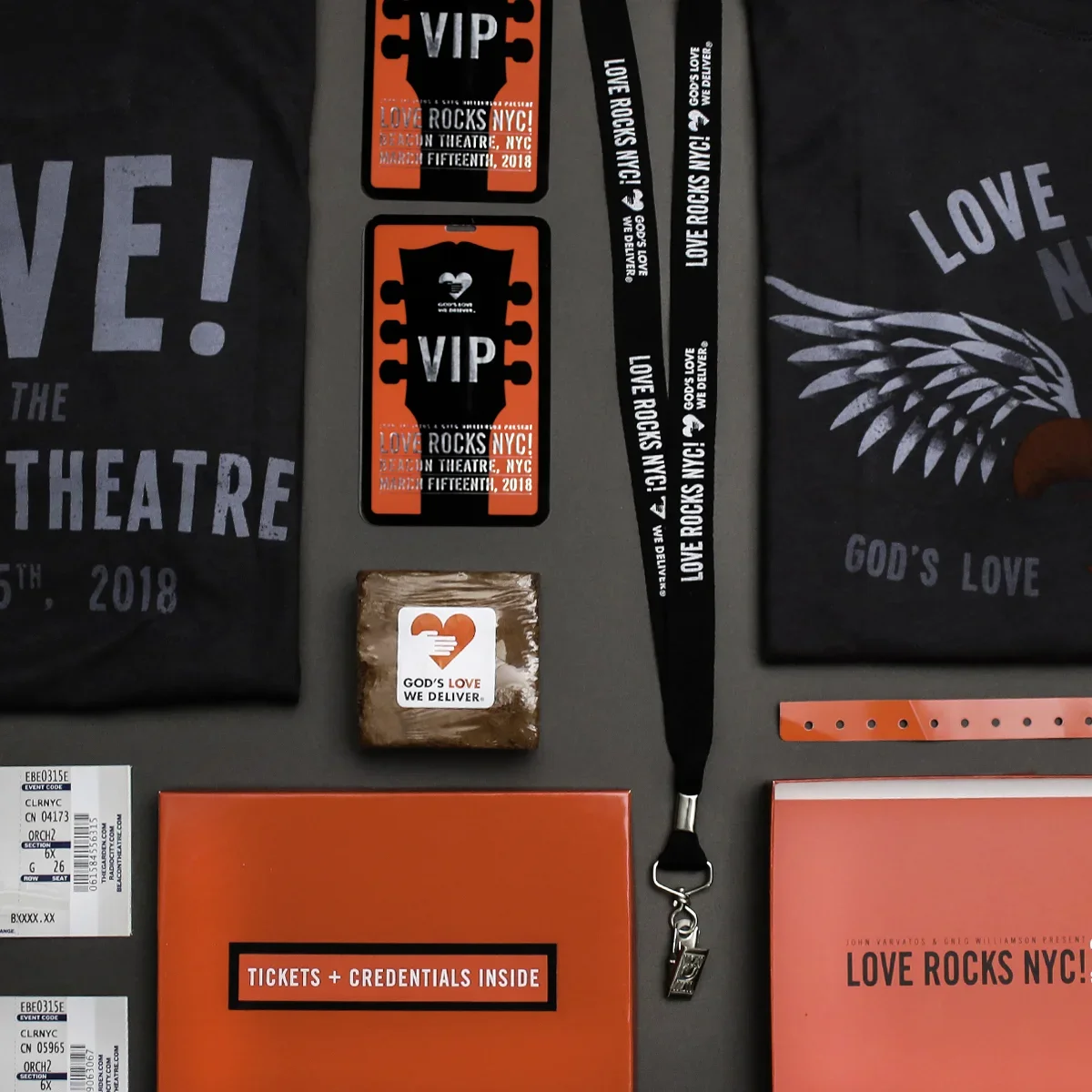 Collection of event badges, wristbands, and tickets for the Love Rocks NYC concert in March 2018. The items feature red, black, and white colors with messages like "VIP," "God's Love We Deliver," and event details. Also visible is a lanyard with the 