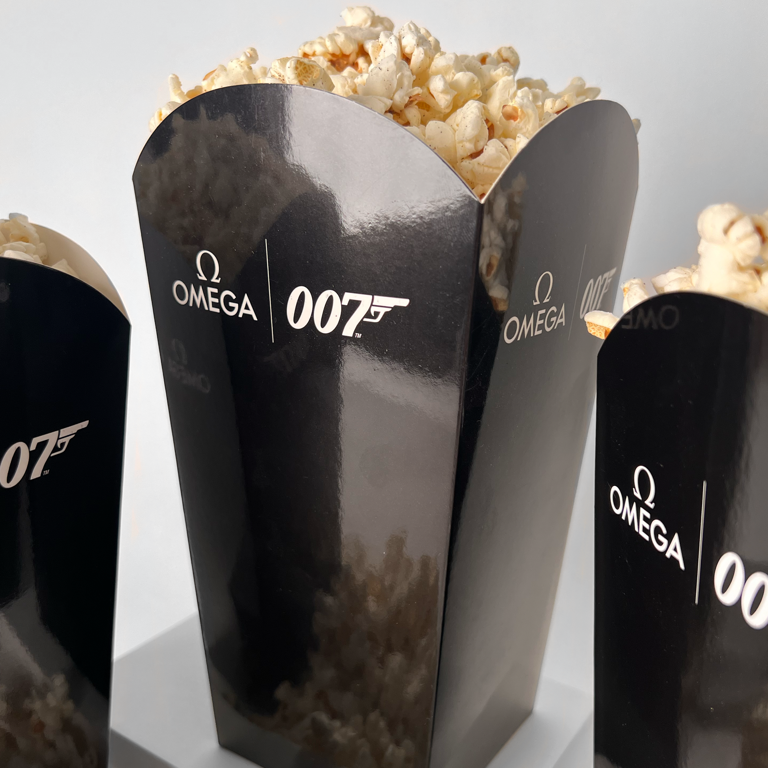Three black boxes with the James Bond 007 logo and Omega logo, filled with popcorn.