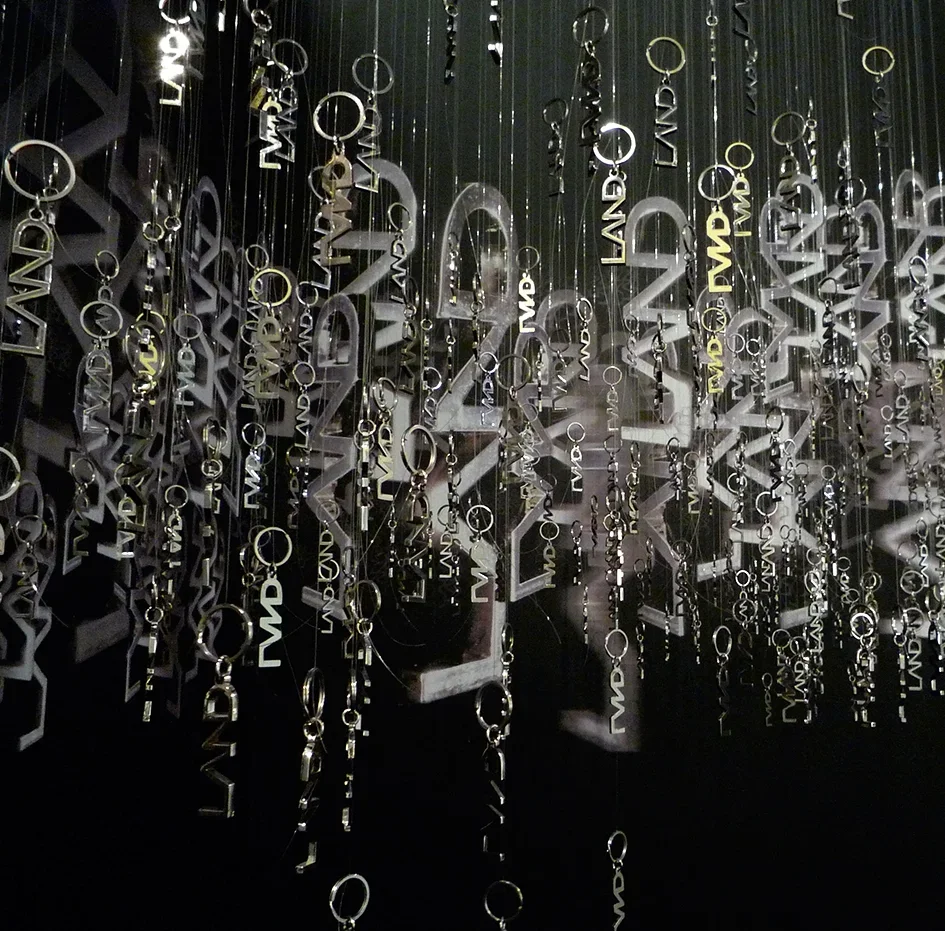 Multiple silver jewelry keychains and charms hanging on black strings with engravings, suspended against a dark background.