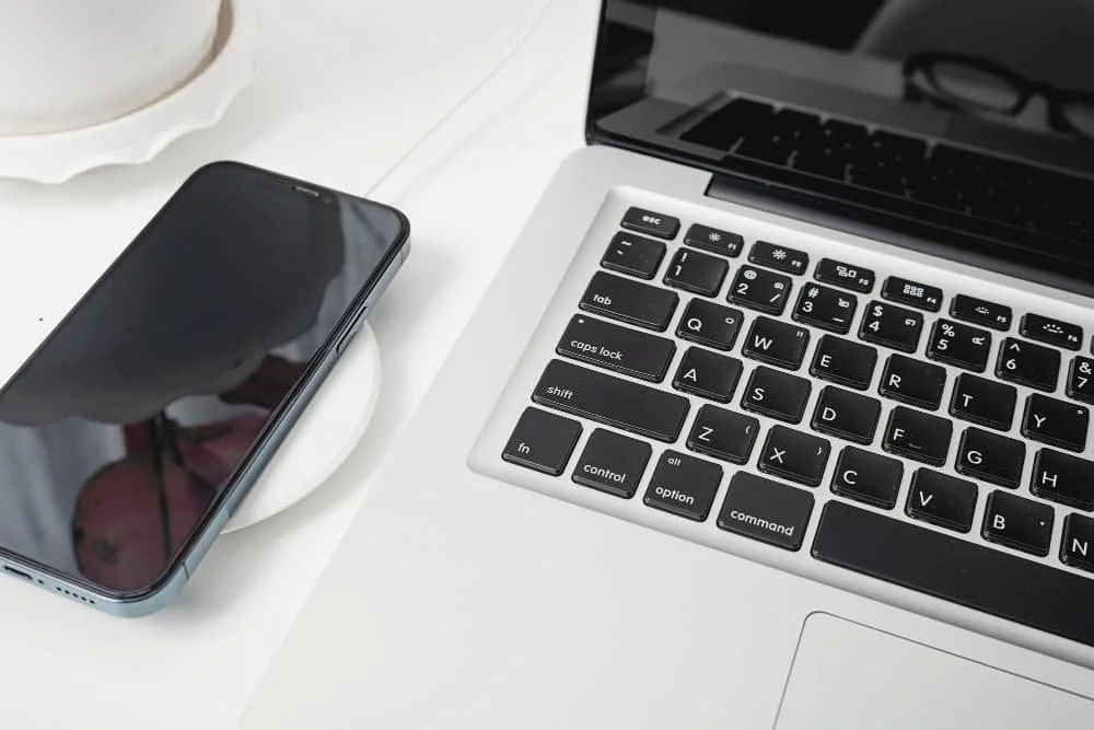 iPhone en una base de carga y un MacBook en una mesa blanca