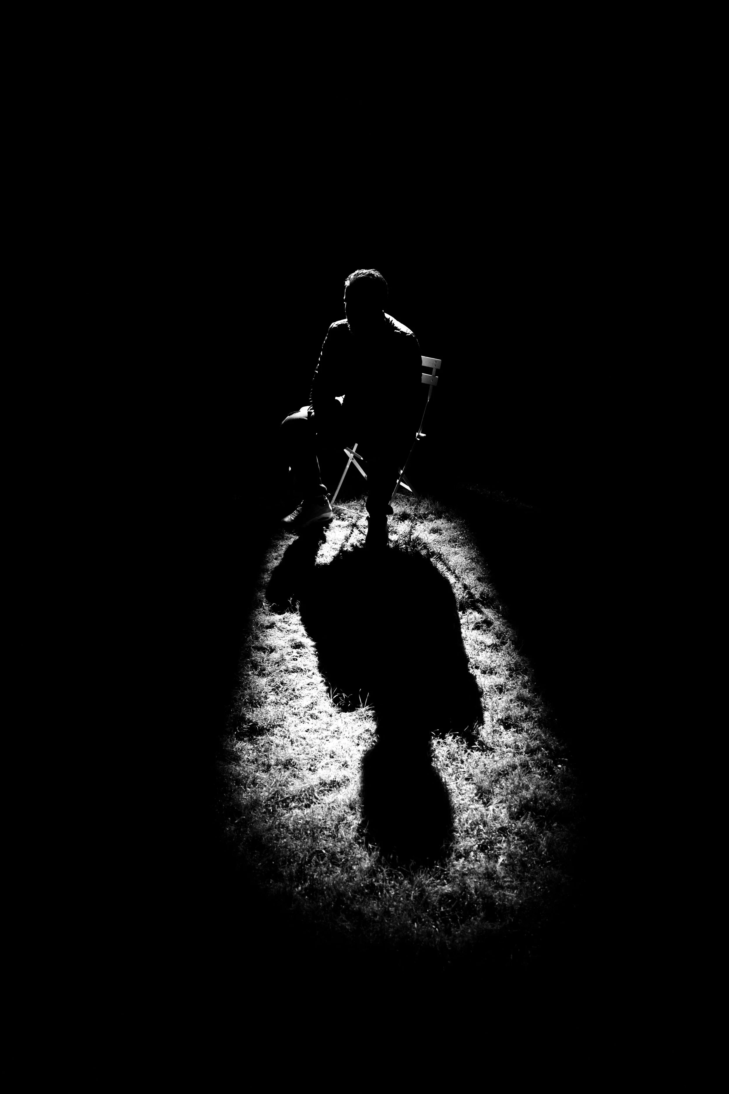Silhouette d'un homme assis sur une chaise, éclairé par une lumière venant de derrière, créant une ombre longue sur le sol.