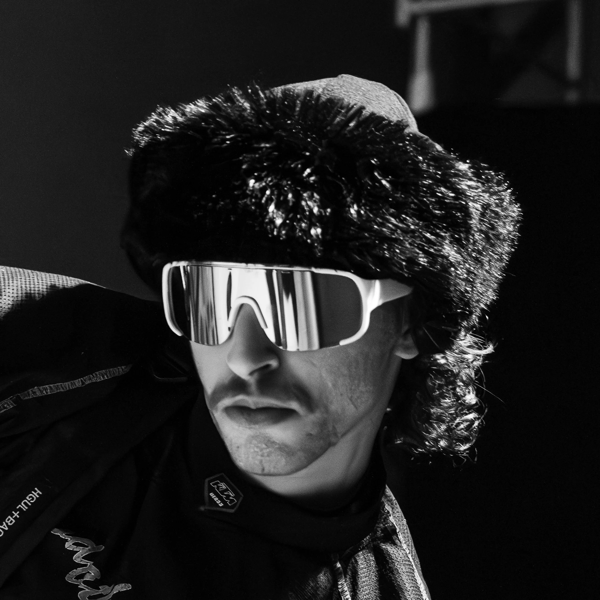 Un homme portant des lunettes de soleil futuristes et un bonnet, regardant vers le côté. Photo en noir et blanc.