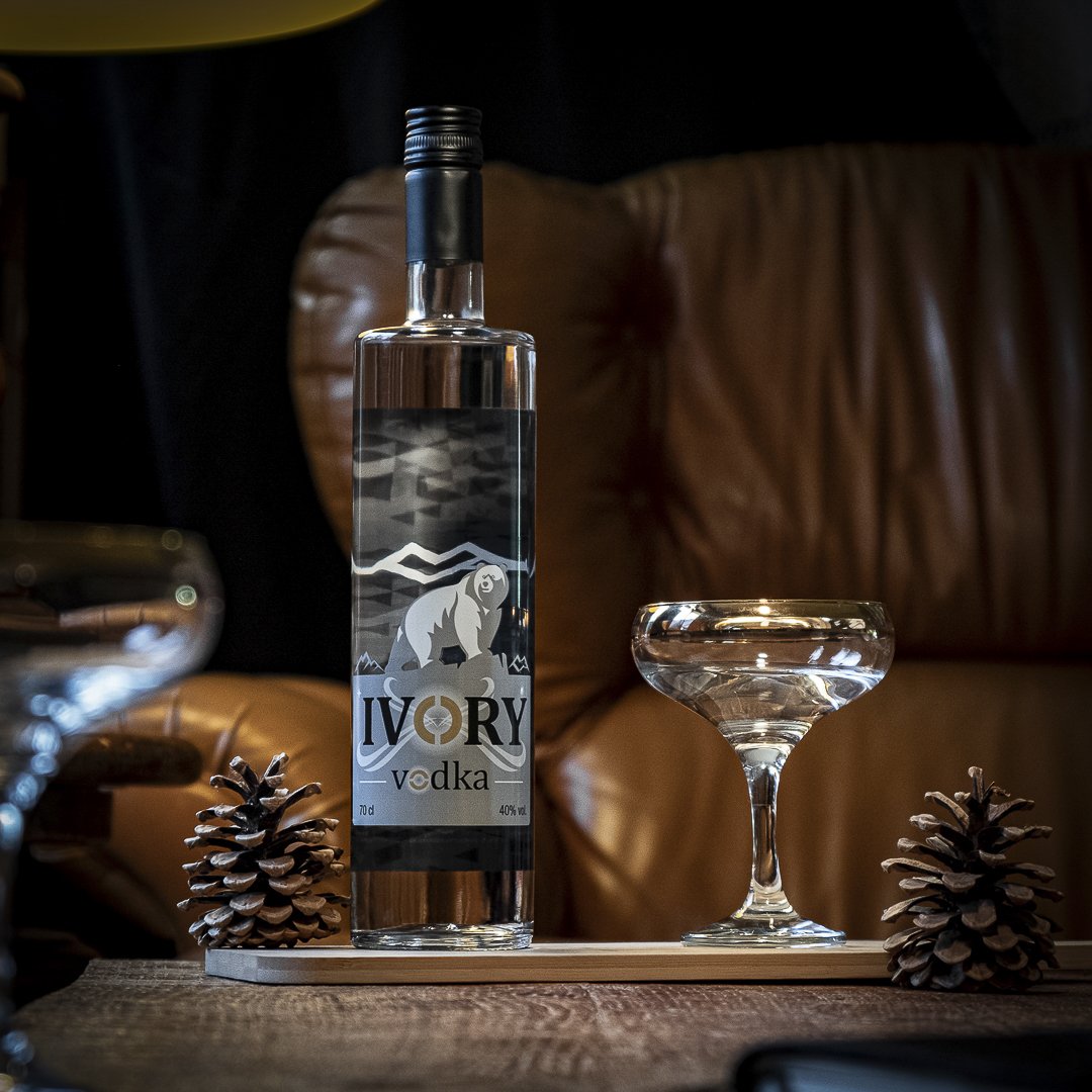 Une bouteille de vodka Ivory, deux pinecones, un verre à cocktail vide, et une planche en bois sur une table en bois