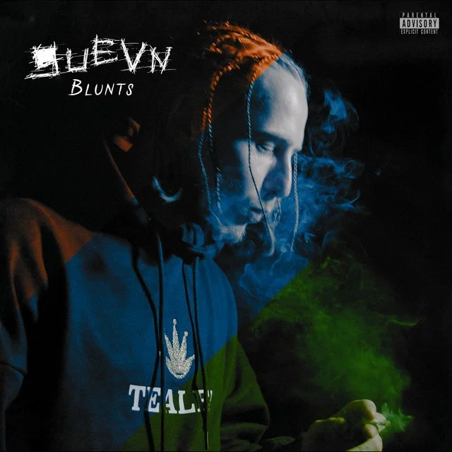 Un homme avec des dreadlocks portant un sweat à capuche, tenant un objet dans la main, avec de la fumée verte et bleue autour de lui, fond sombre.