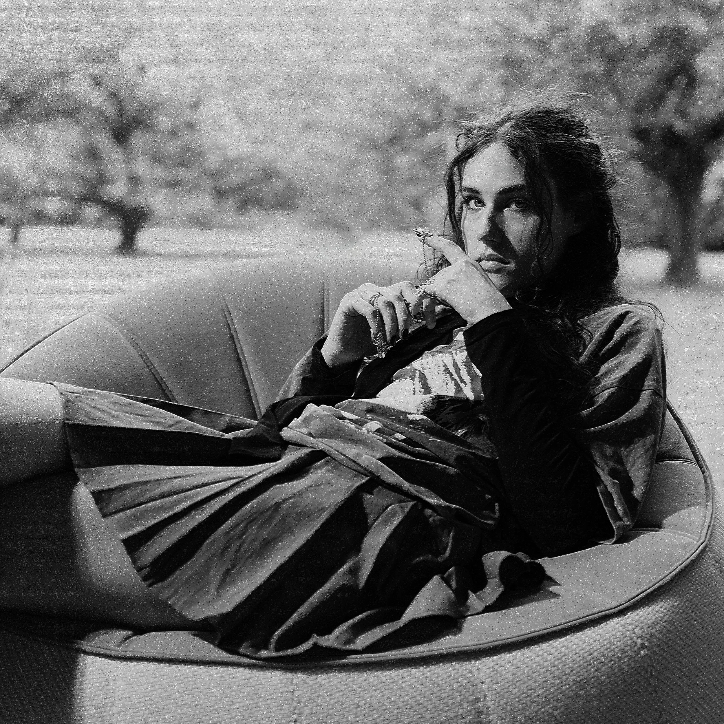 Une femme assise sur un canapé dehors, portant des vêtements décontractés, avec des arbres en arrière-plan.