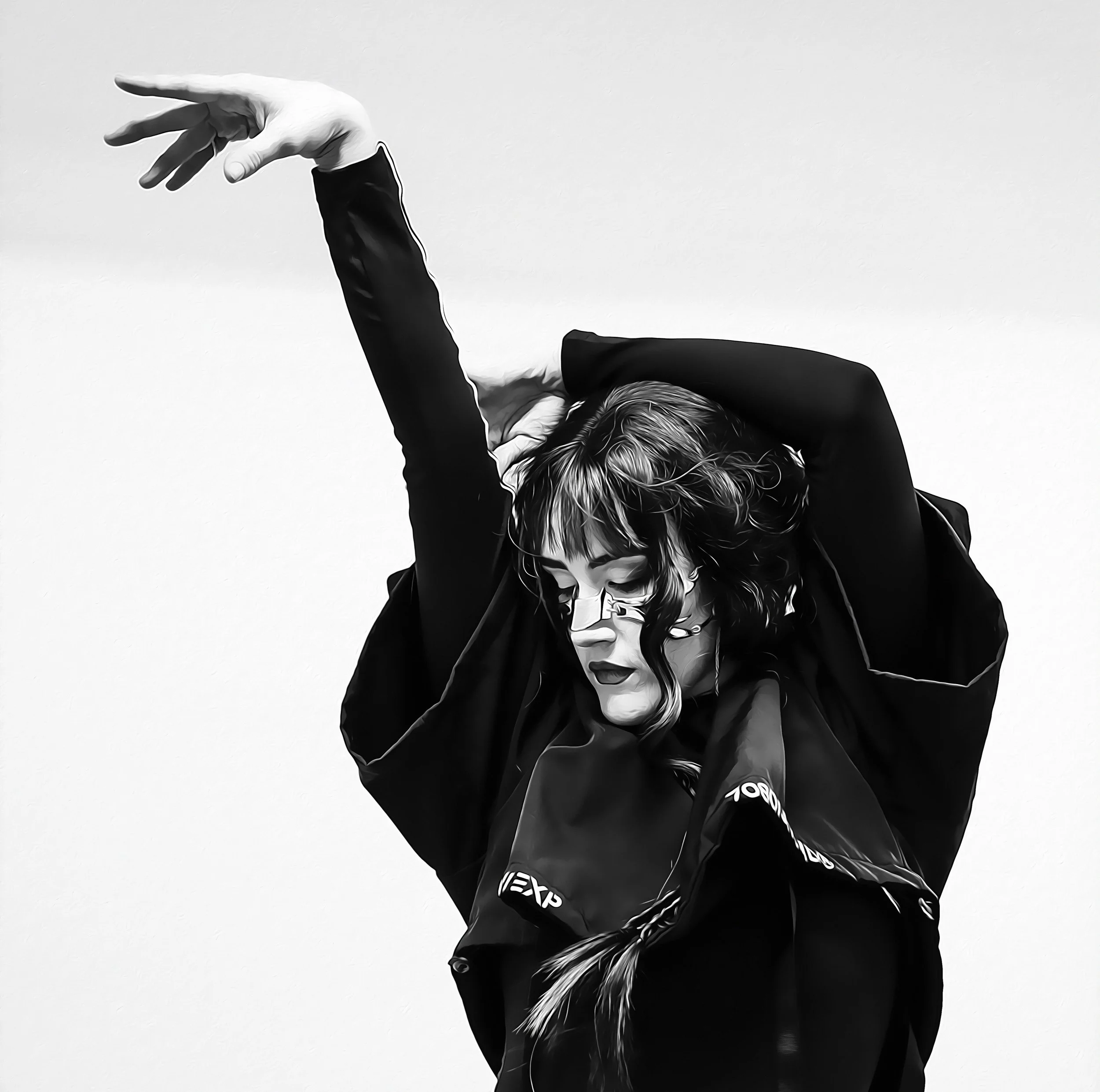 Une femme portant des lunettes, avec des cheveux bouclés, en train de danser ou de poser, vêtue d'une veste noire contre un fond blanc.