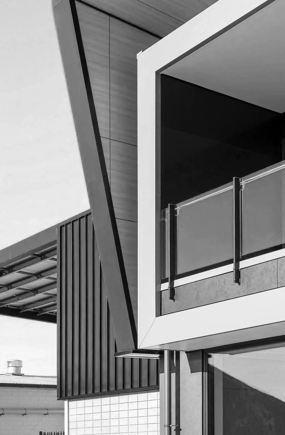 Black and white photo of a modern building with geometric shapes, glass balcony, and metal siding.