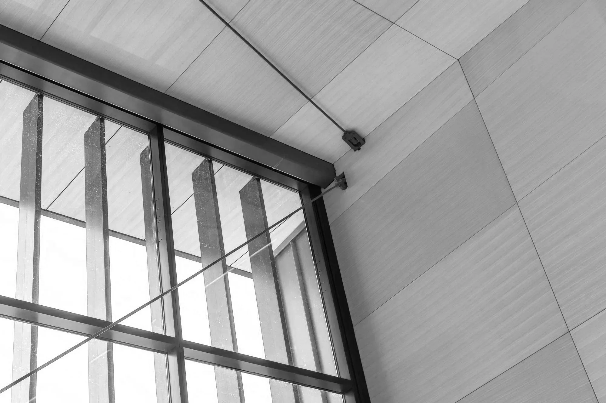 Interior view of a modern building with large glass windows and wood-paneled walls, with visible metal supports and a cable or wire.