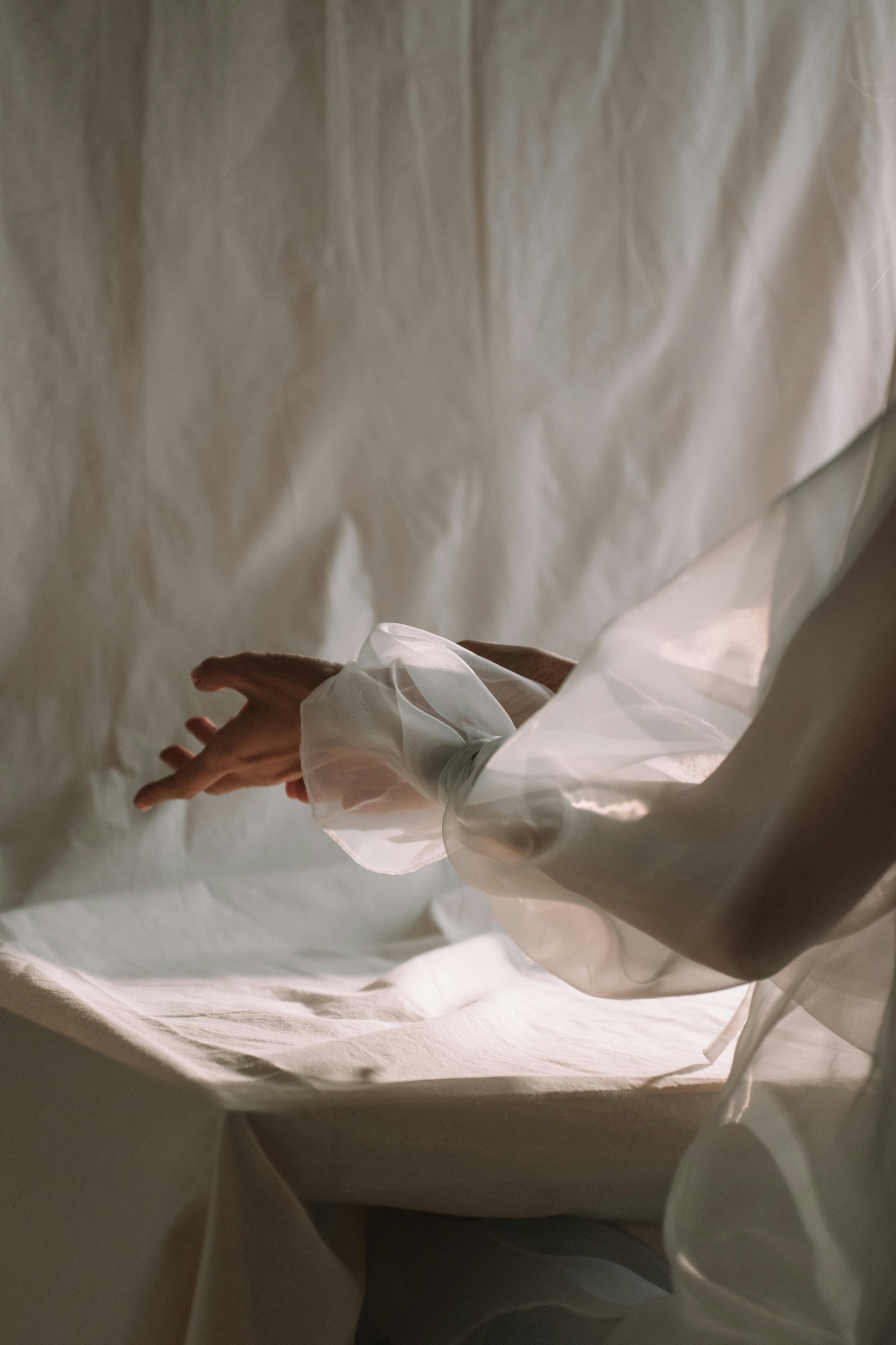 Main d'une personne portant une chemise en tissu transparent, tenant délicatement une autre main. Fond neutre, éclairage doux.