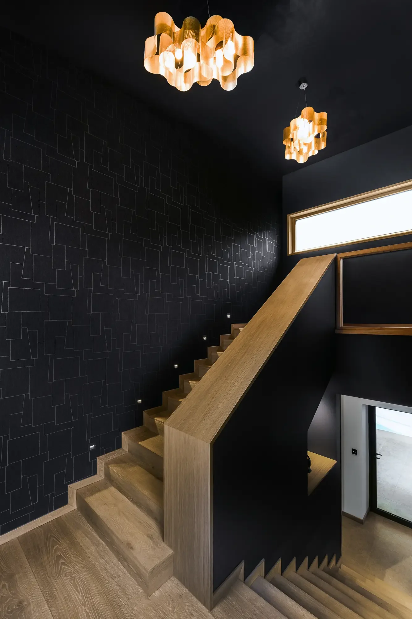Escalier en bois avec rampe en bois clair dans une pièce sombre avec murs noirs et design moderne, éclairage suspendu en forme de nuage en bois.