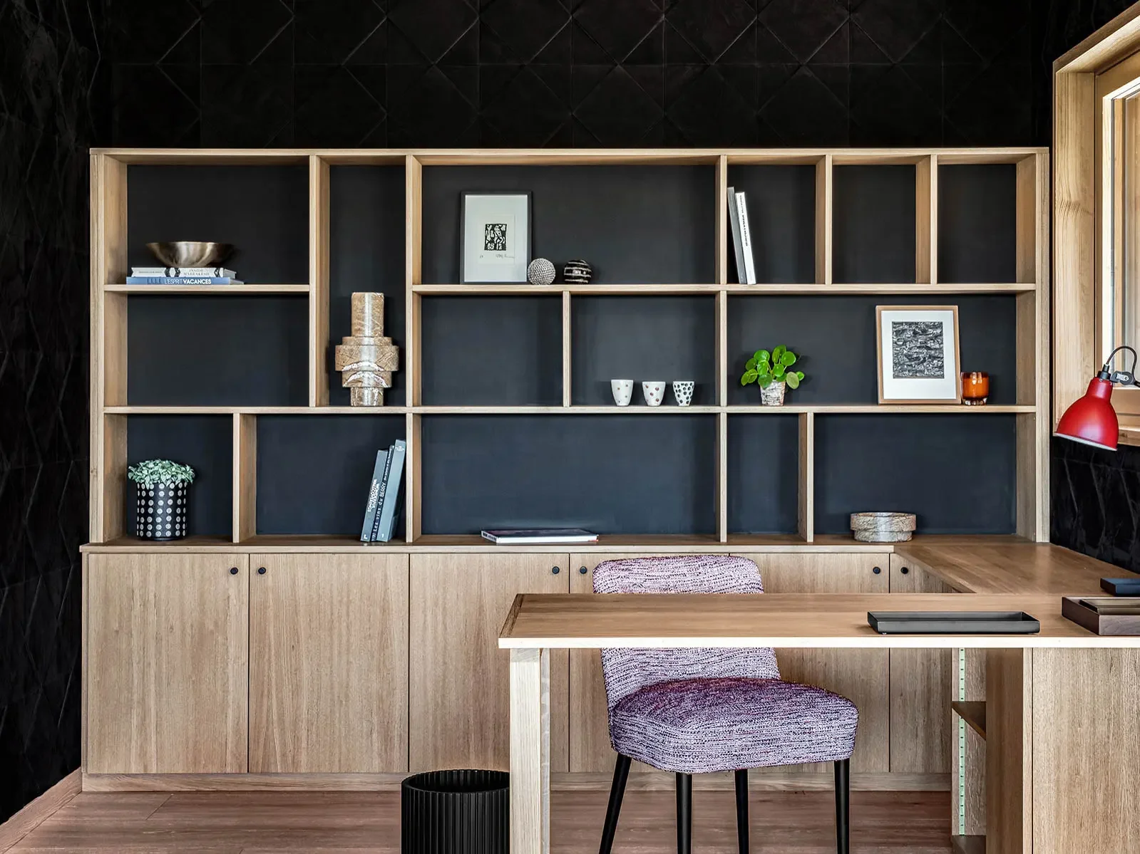 Etagère en bois avec plusieurs compartiments noirs décorés de livres, vases, photo et plantes, dans un bureau moderne avec bureau en bois et chaise rembourrée