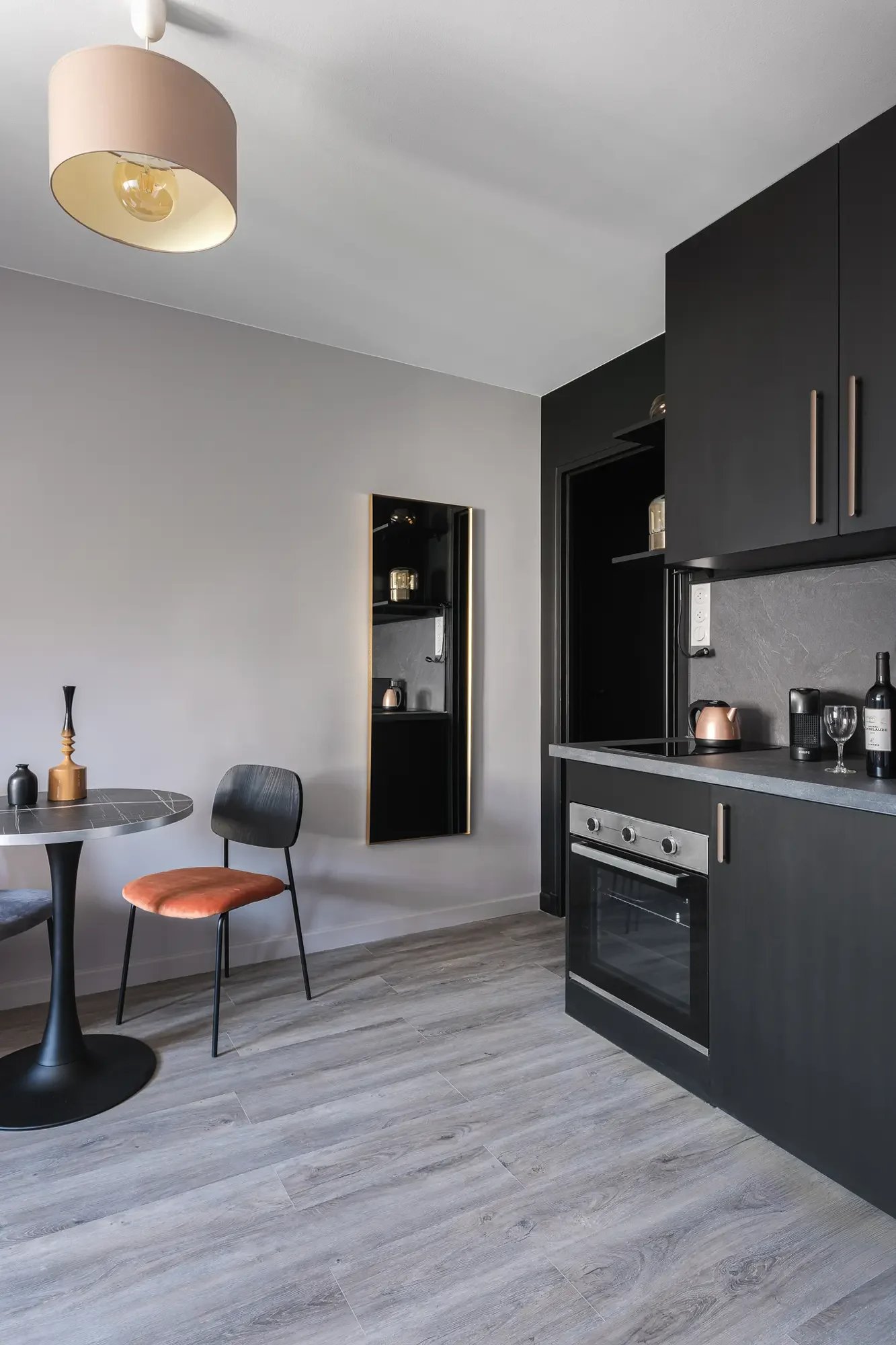 Cuisine moderne avec meuble noir, four intégré, petite table ronde, deux chaises, décor minimaliste et reflet dans un miroir