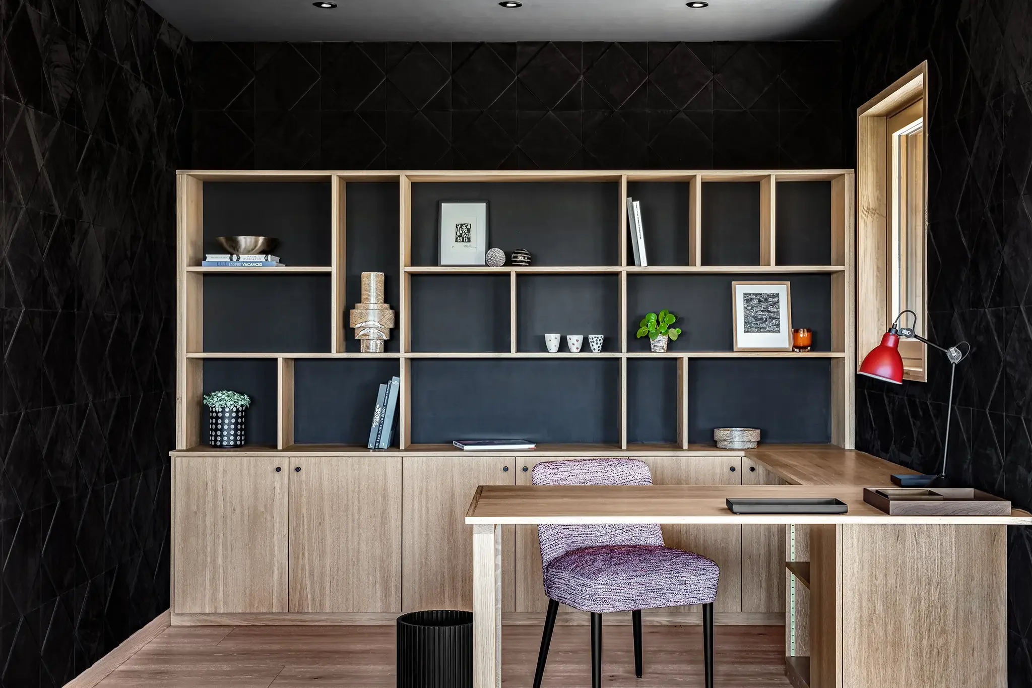 Bureau avec étagère en bois clair, mur cuir noir derrière, décoration avec plantes, cadres, livres, et objets décoratifs, bureau avec chaise bouclette dans une pièce moderne.