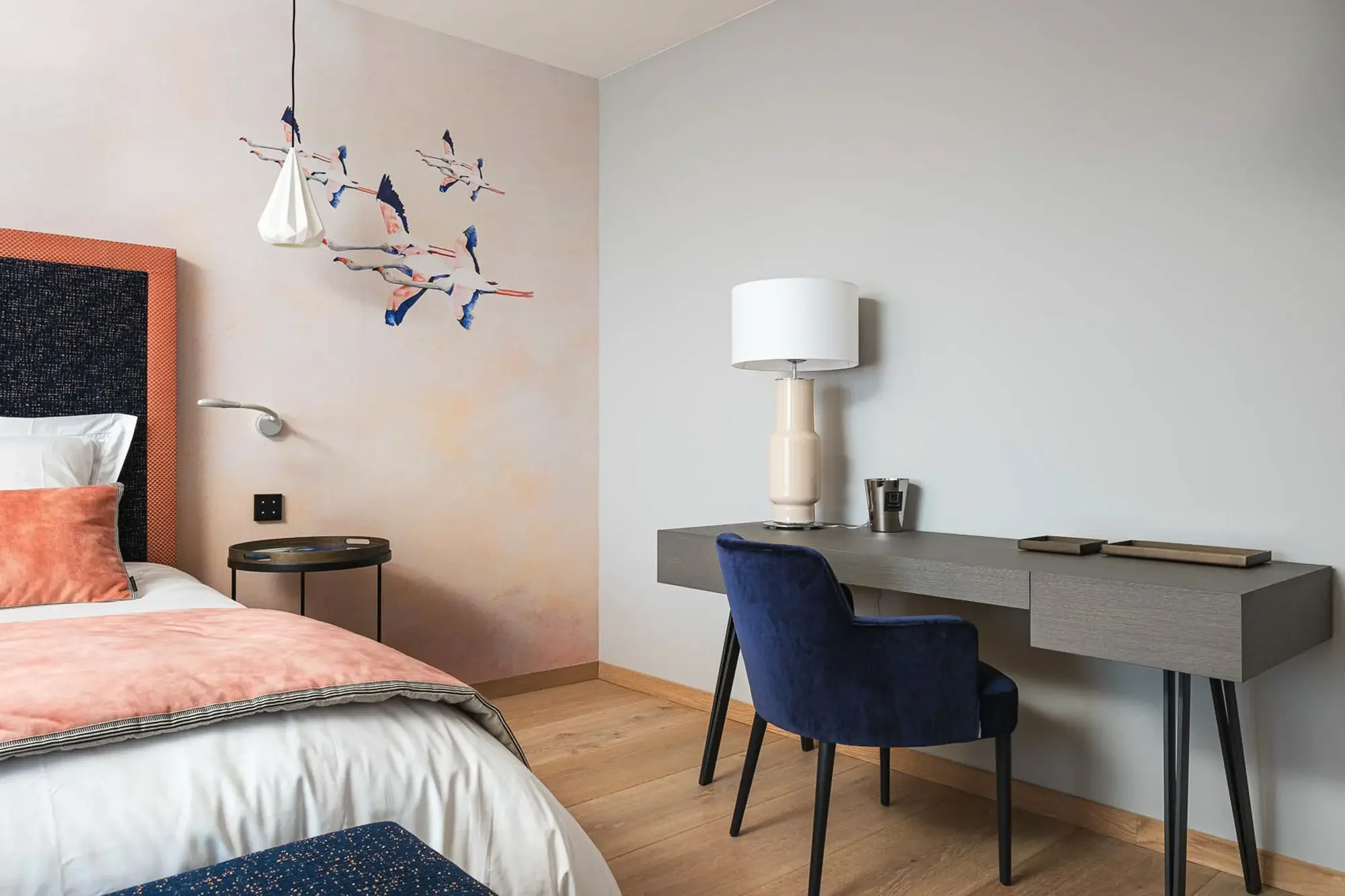 Chambre moderne avec un lit, une lampe de chevet, un bureau avec une lampe, une table en verre, et une décoration murale avec des oiseaux