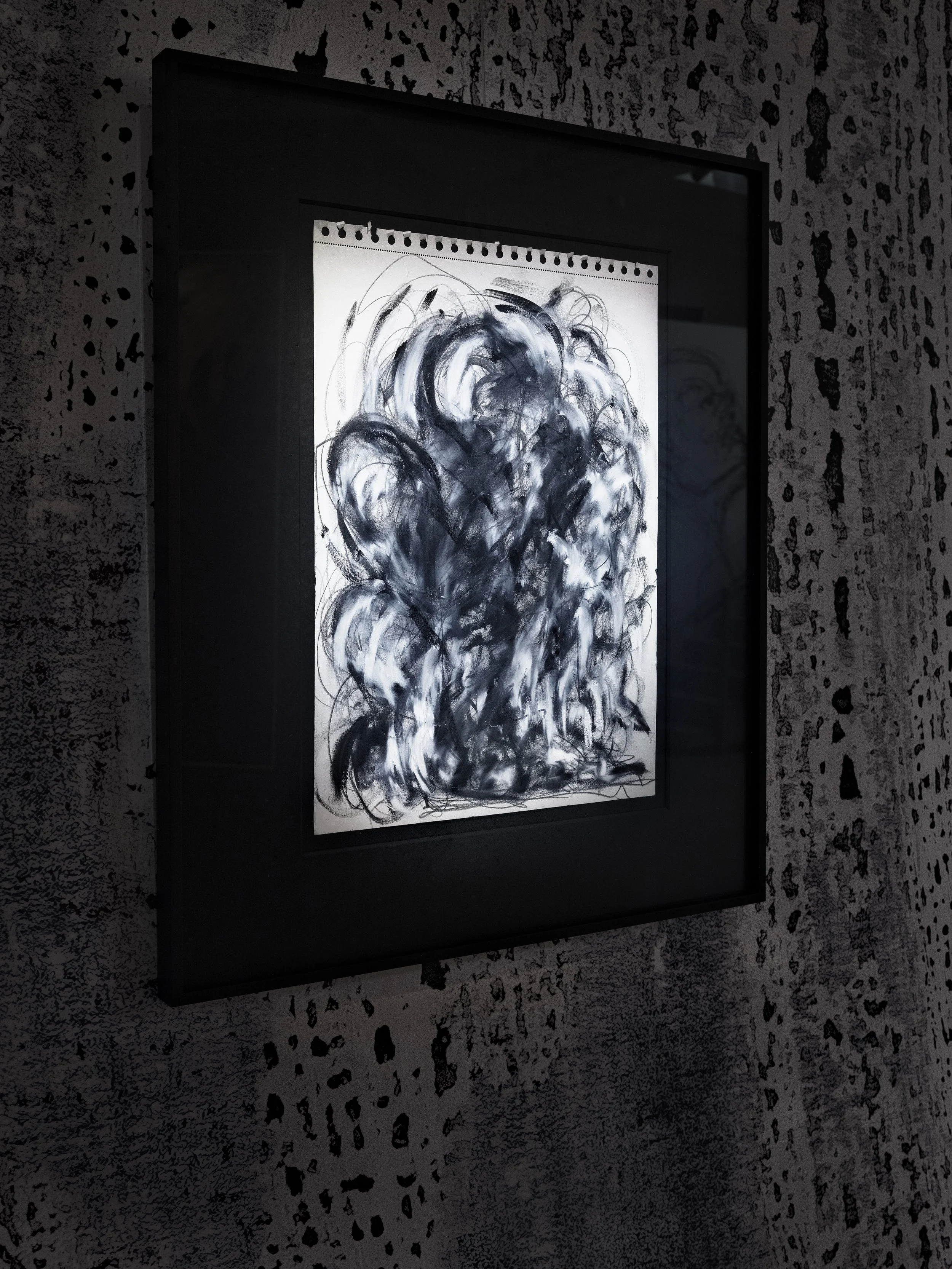 Une œuvre d'art abstraite en noir et blanc encadrée, avec des coups de pinceau fluides et tourbillonnants, exposée sur un mur à motif texturé.