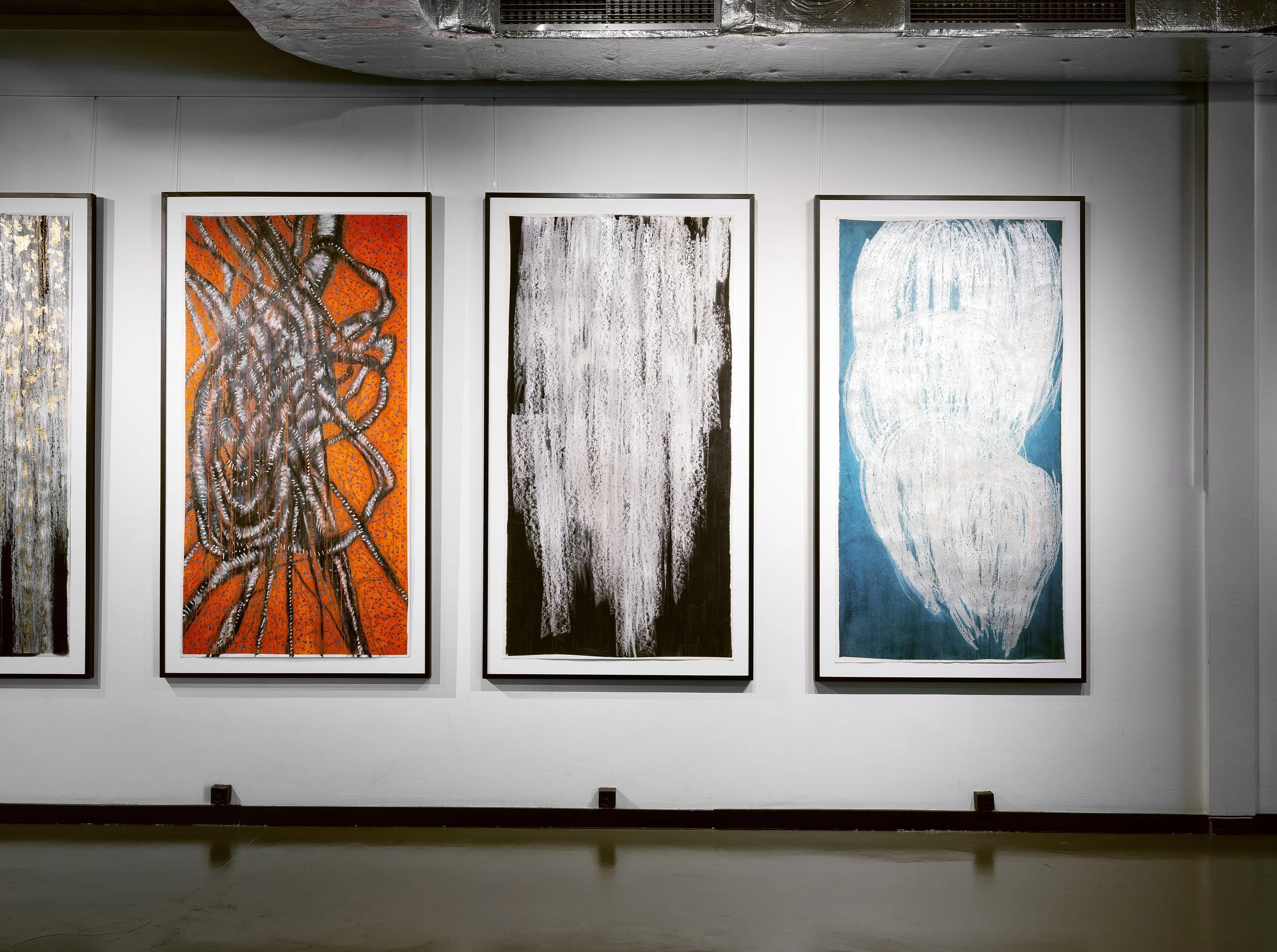 Trois tableaux abstraits exposés sur un mur blanc dans une galerie d'art.