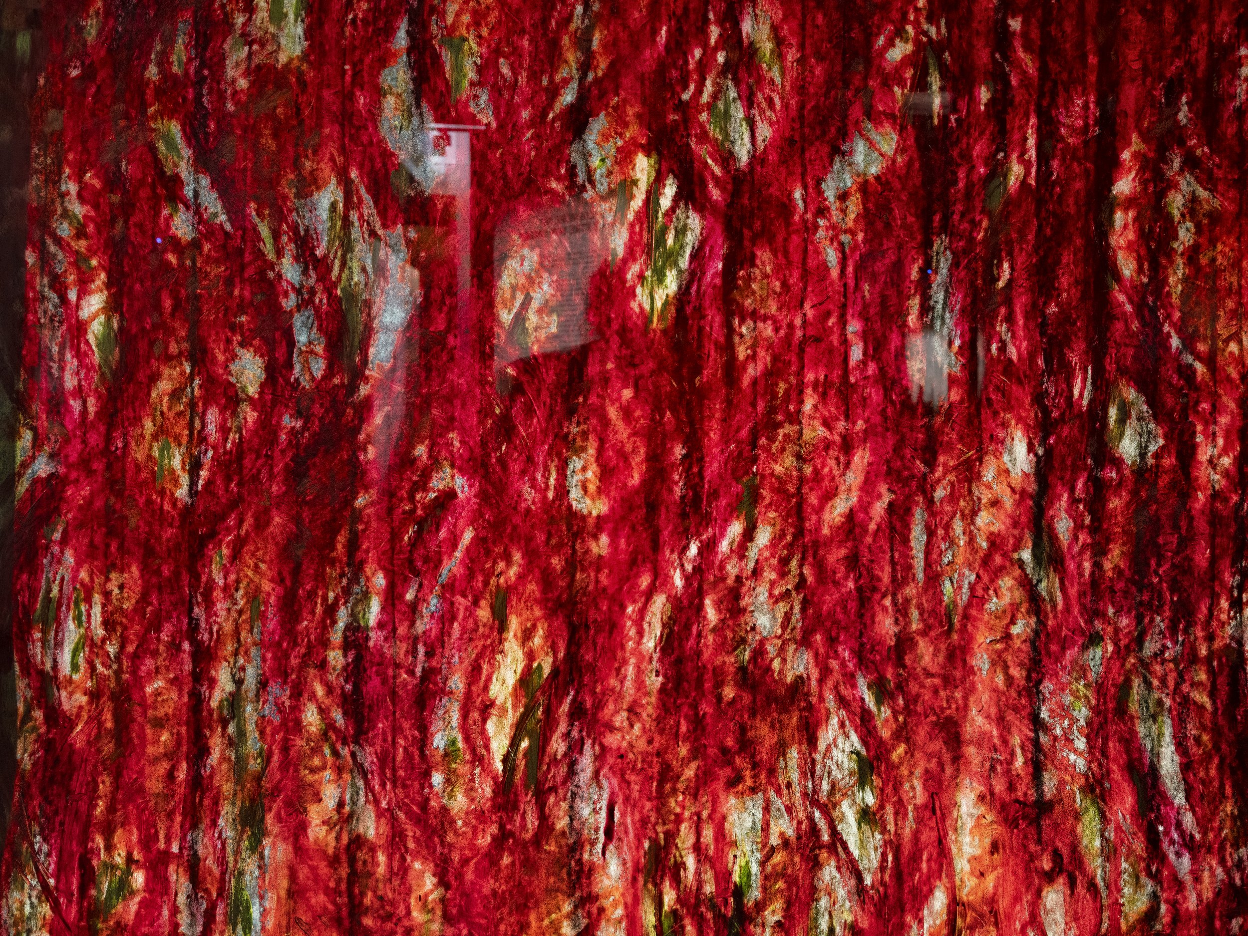 Une peinture abstraite avec principalement des nuances de rouge, avec quelques touches de vert, blanc et beige.