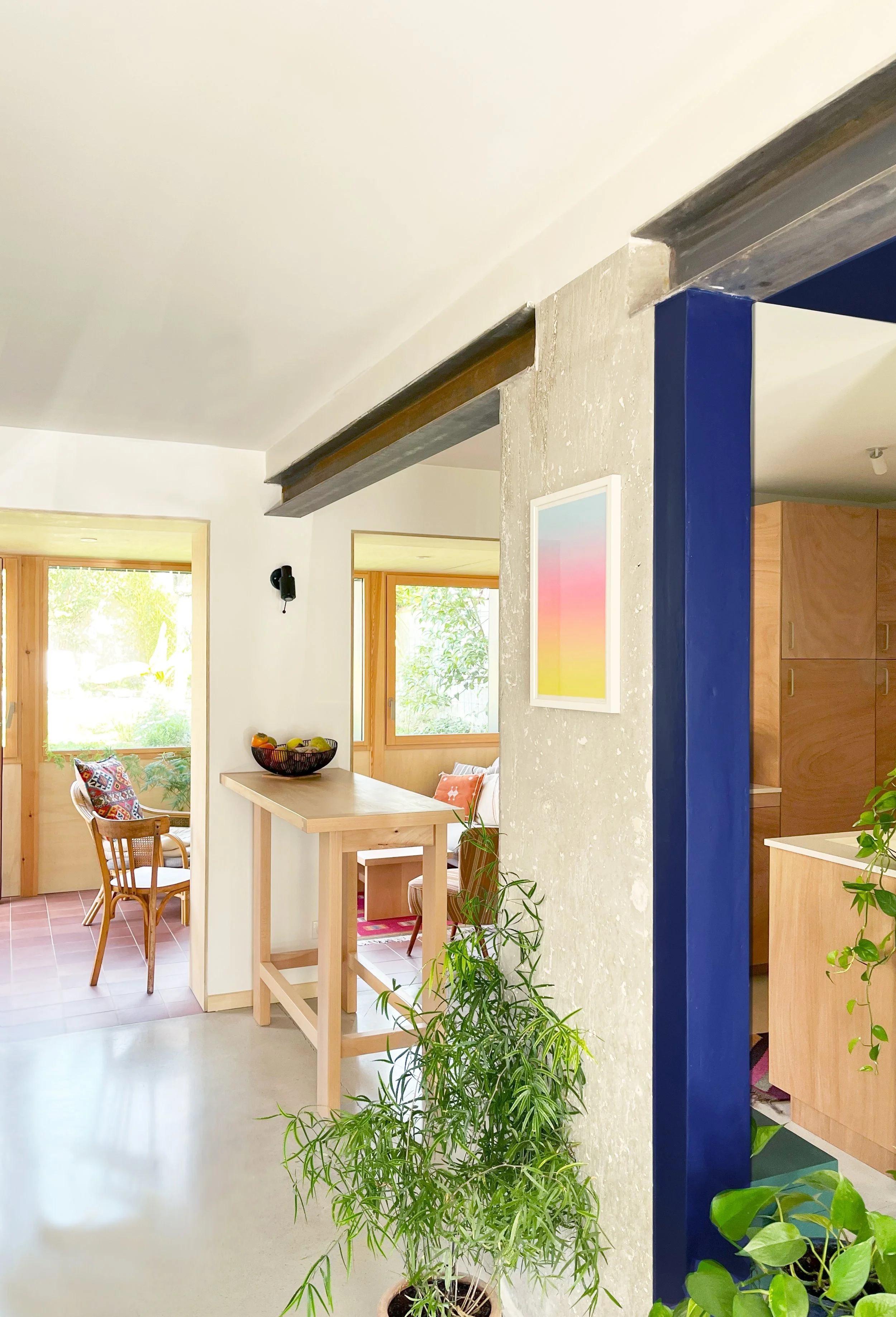 Intérieur d'une maison avec meubles en bois, plantes vertes, fenêtres lumineuses, et décoration moderne.