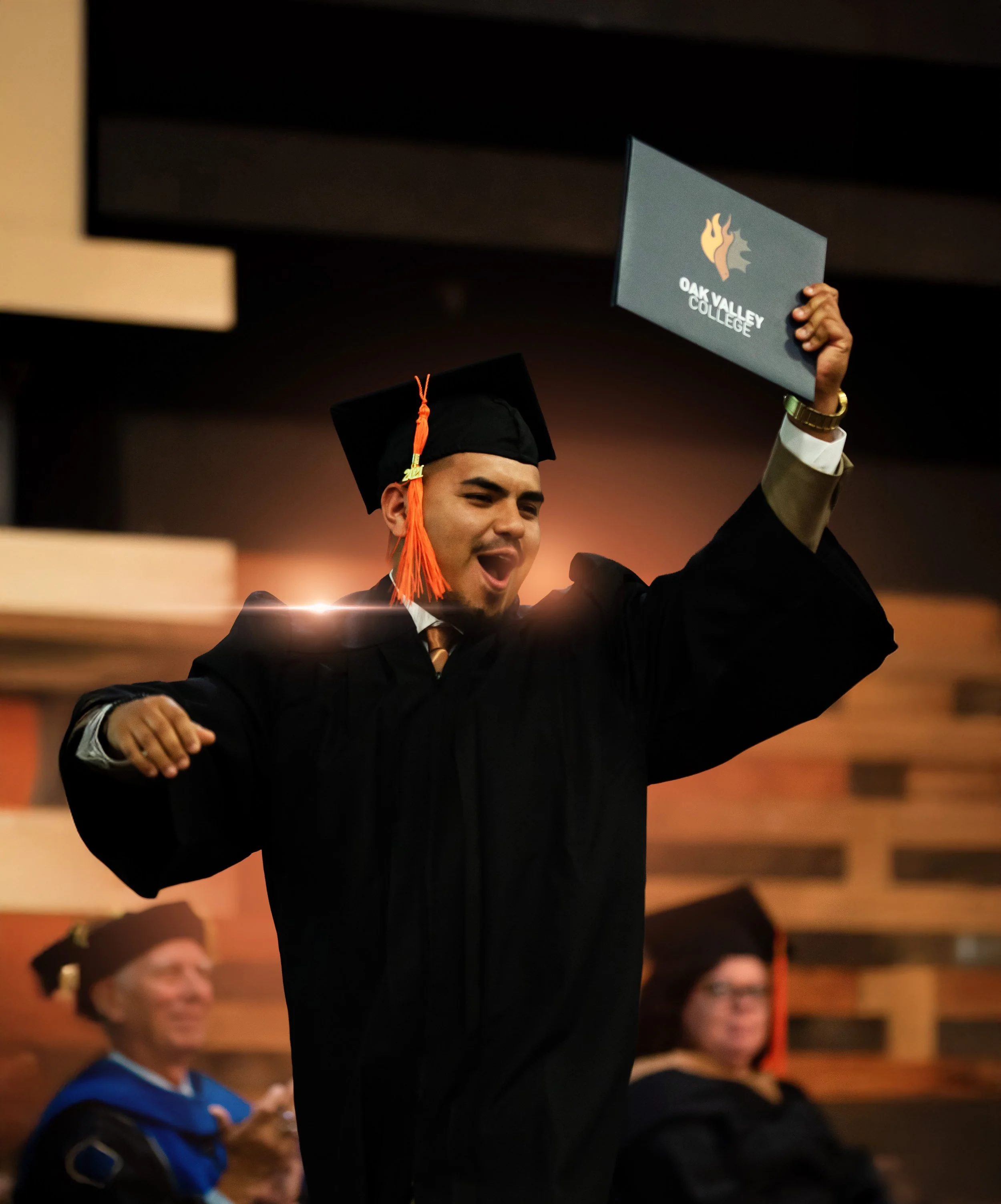 Happy graduate in cap and gown celebrating during graduation ceremony, holding diploma from Oak Valley College.