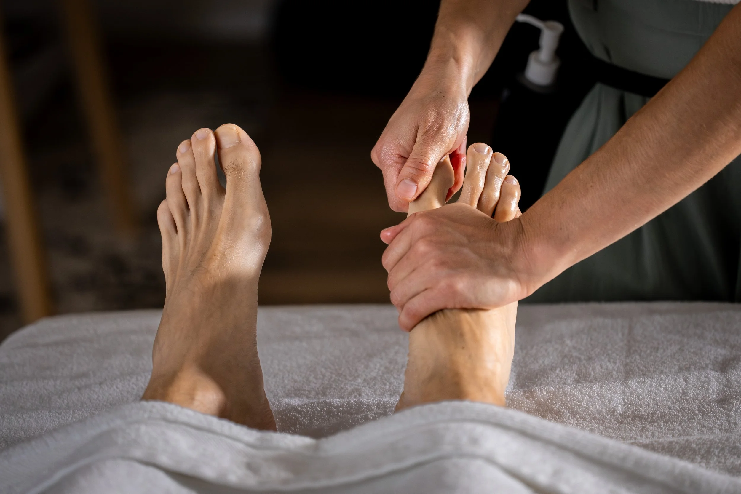 Personne recevant un massage du pied. Etirement doux du gros orteil du pied droit. Avec une main, la masseuse maintient les articulations à la base des orteils, pour pouvoir réaliser l'étirement et le lissage du gros orteil avec l'autre main. 