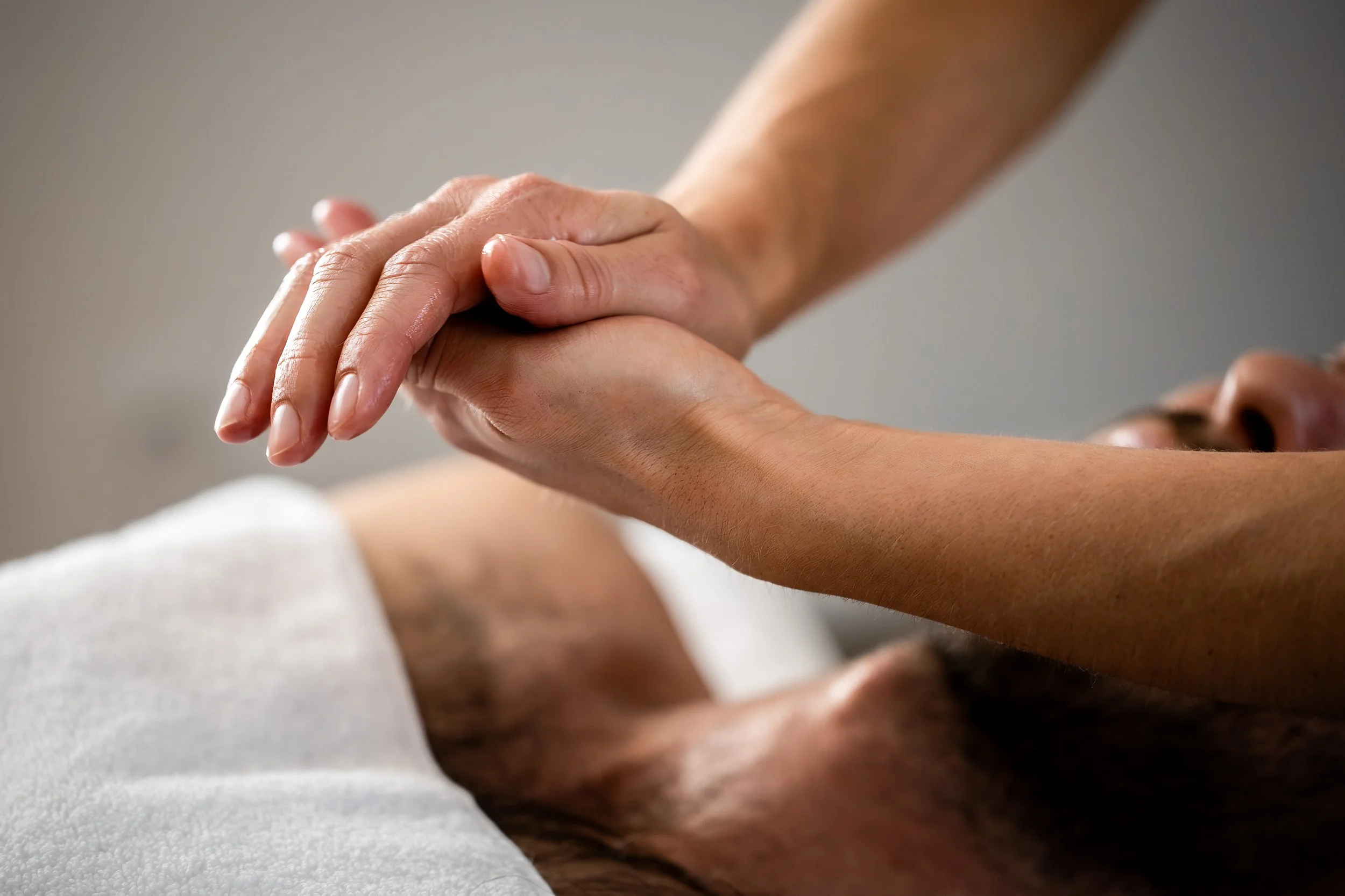 Une masseuse récupère de l'huile de massage entre ses mains. Un personne massée se trouve en arrière plan, alors que les mains sont en gros plan. 