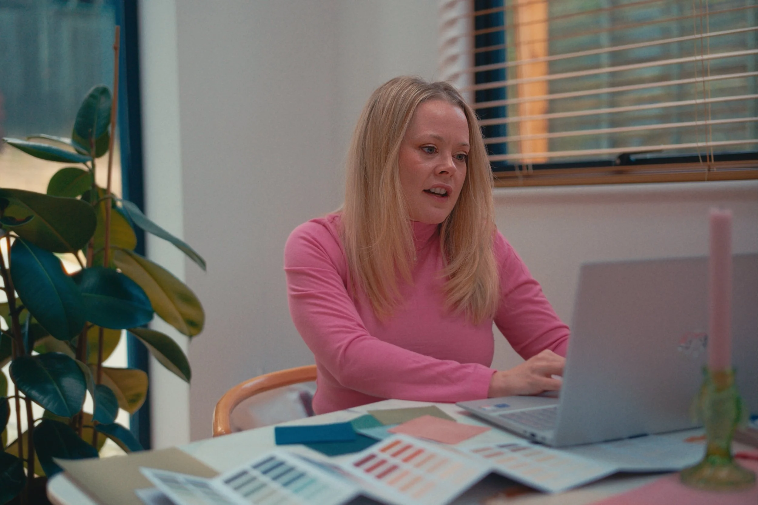 Lucy is working at her laptop surrounded by plans and colour swatches