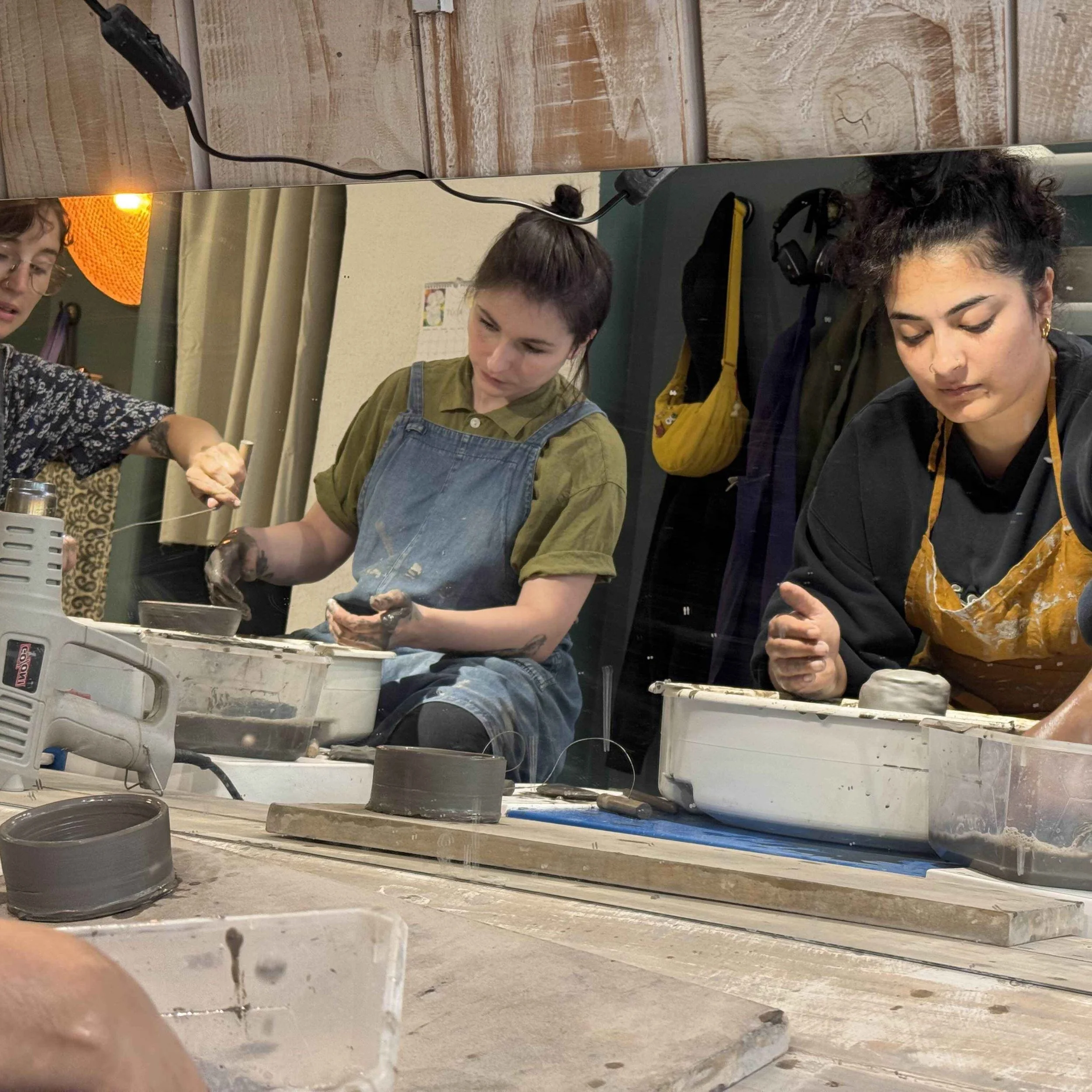 Two women and a person collaborate on a pottery project, shaping clay at a ceramics workshop.
