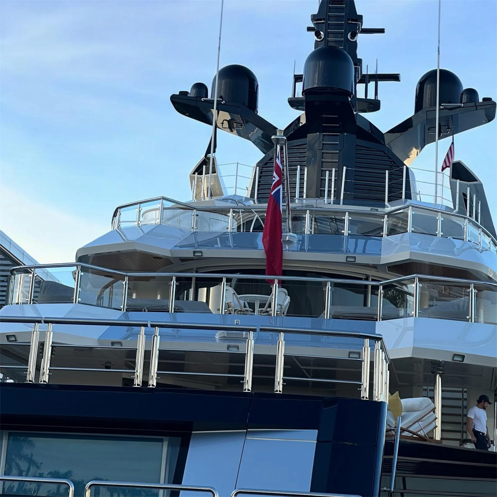 Close-up of the upper deck and bridge of a luxury yacht with multiple outdoor seating areas, flags, and navigation equipment against a blue sky.