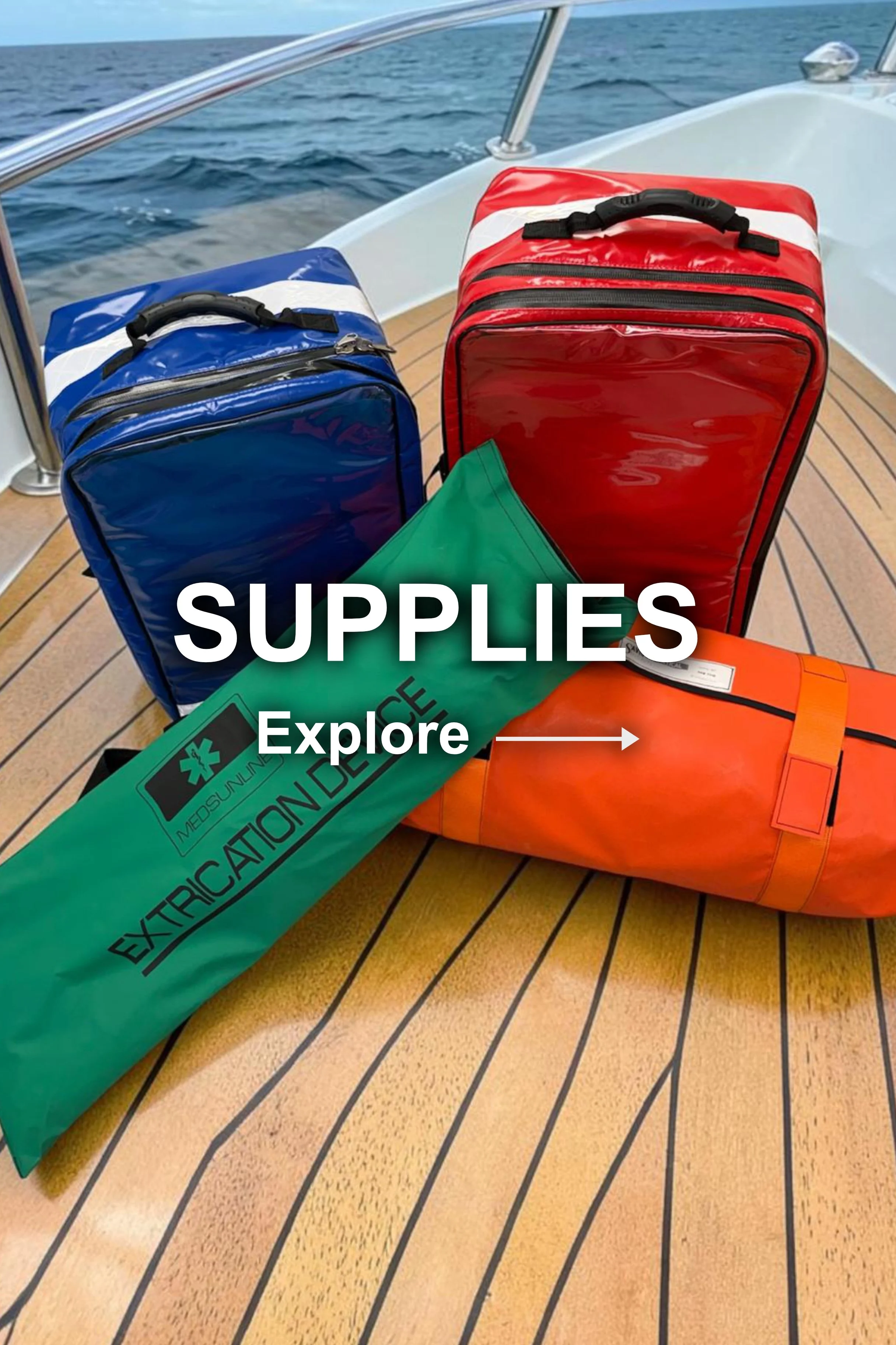 On a boat deck, sitting on wood laminate flooring, are two large colorfully labeled bags: one blue and one red, with a green bag and orange emergency item nearby. The background shows the ocean water.