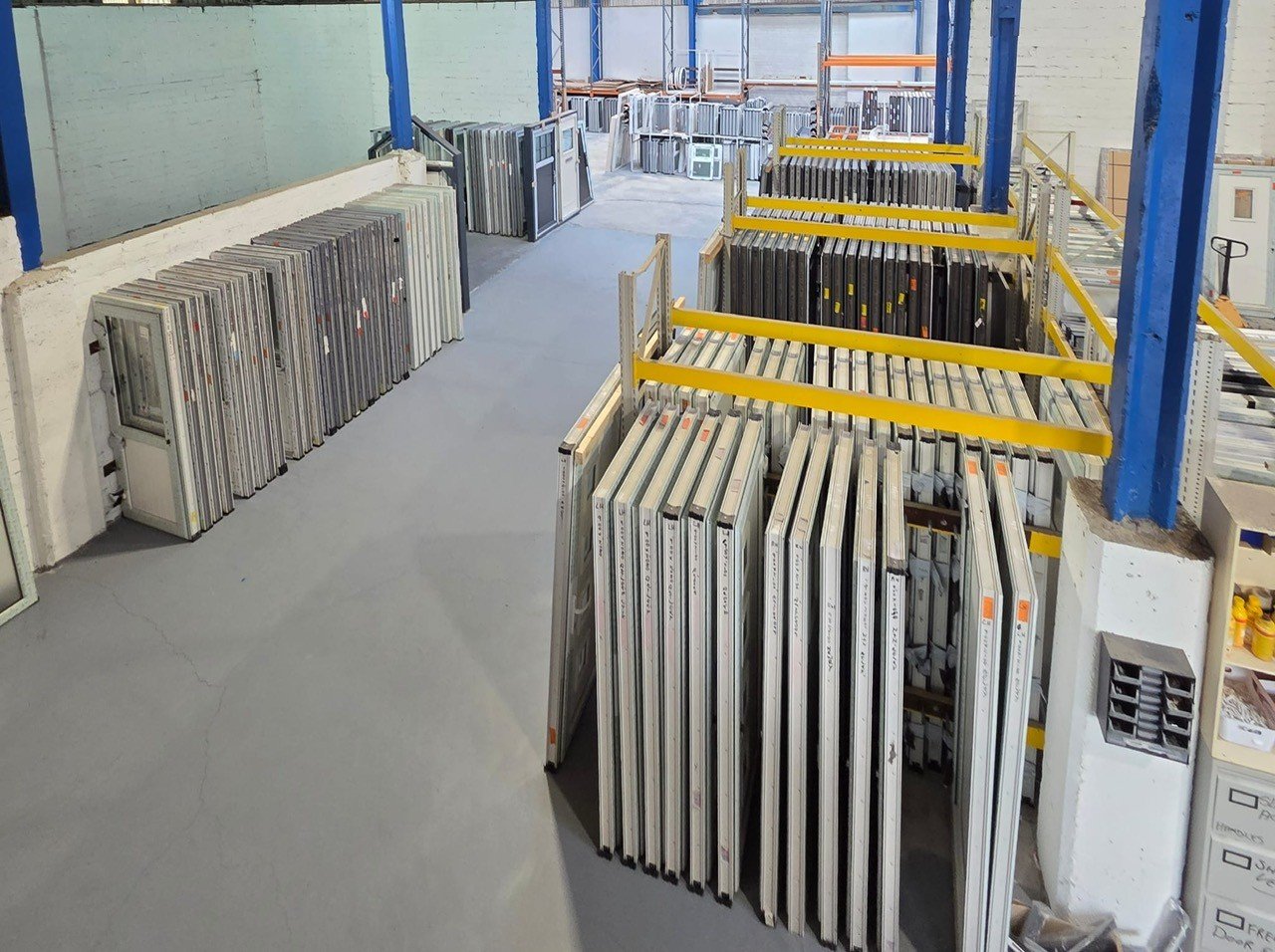 Store interior with metal shelving holding window frames and glass panels, likely a glass or window supply store.