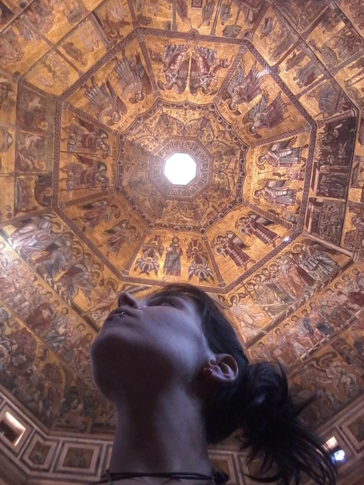 Ragazza che guarda verso l'alto in un interno con soffitto decorato a mosaico dorato.
