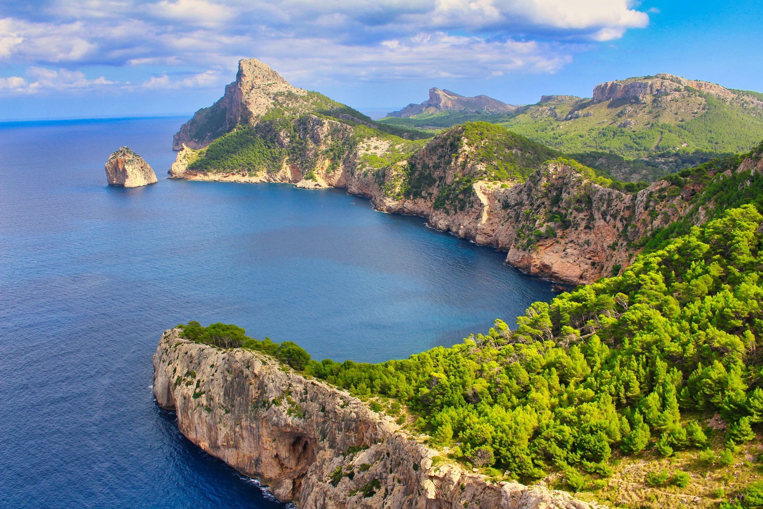 Aerial view of coastal cliffs with green vegetation, blue water, and partly cloudy sky.