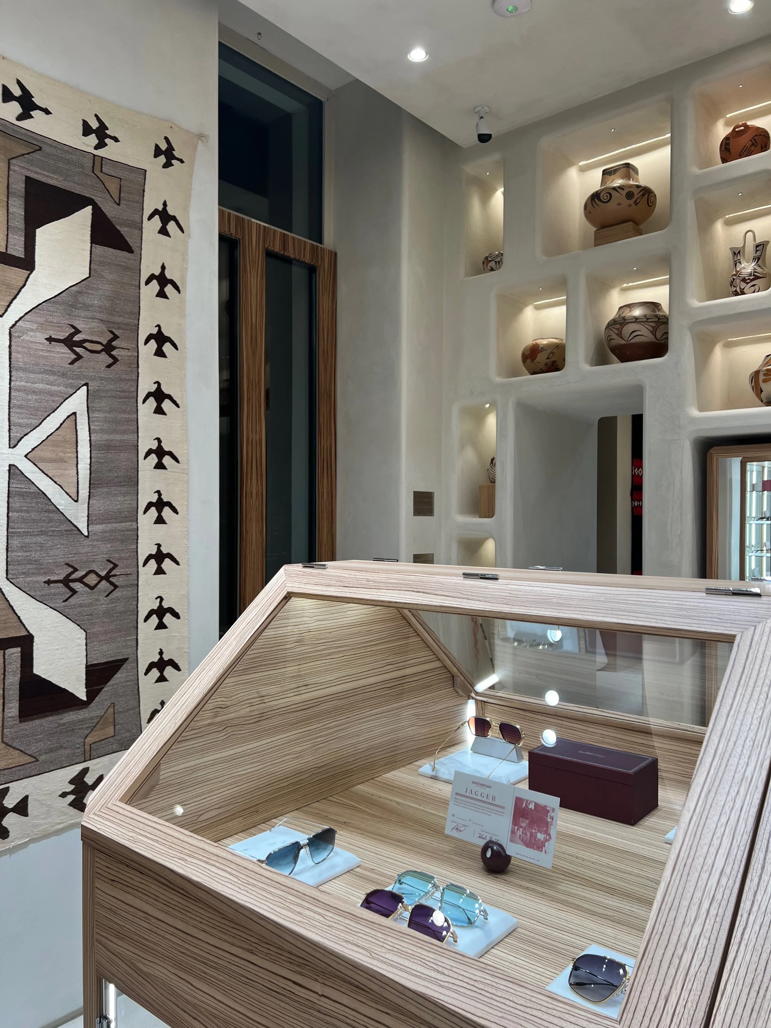 Interior of a store showcasing a glass display case with sunglasses and accessories, decorated with pottery and woven wall hangings.