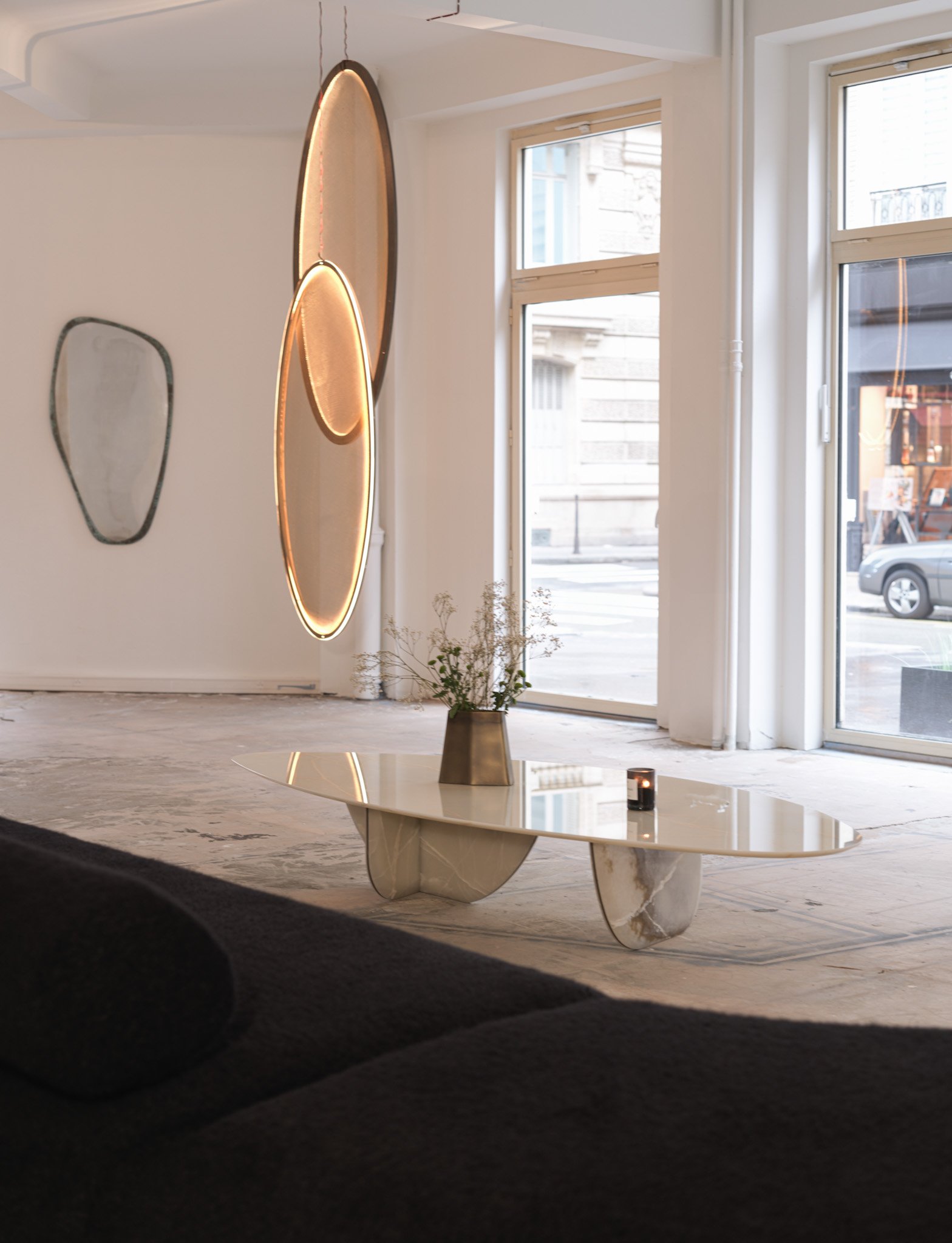 Modern interior with abstract wall art, a marble coffee table with a vase and candle, and large windows letting in natural light.