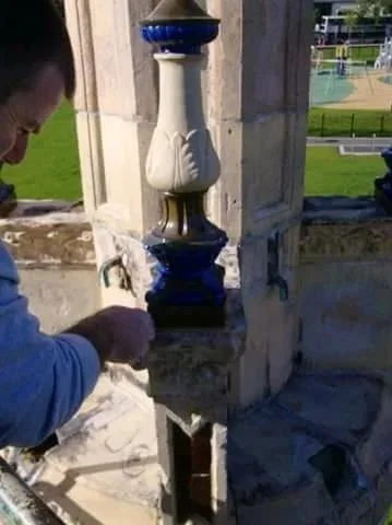 Person working on a stone or marble fountain with a decorative blue and white ceramic piece outside.