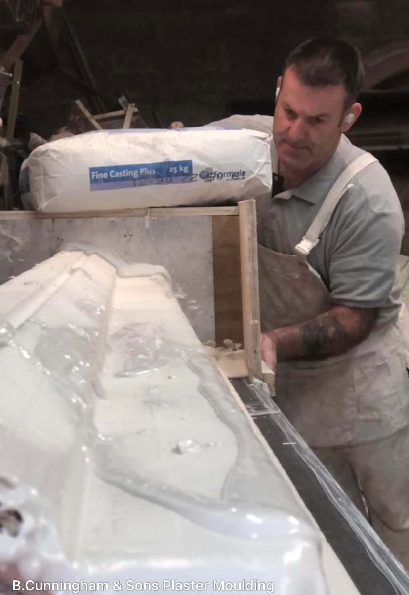 A man working on a plaster mold with a large bag labeled 'Fine Casting Plus' in a workshop setting.