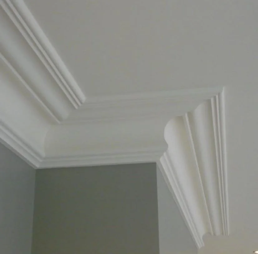 Ceiling corner with decorative white crown molding in a room with grey walls.