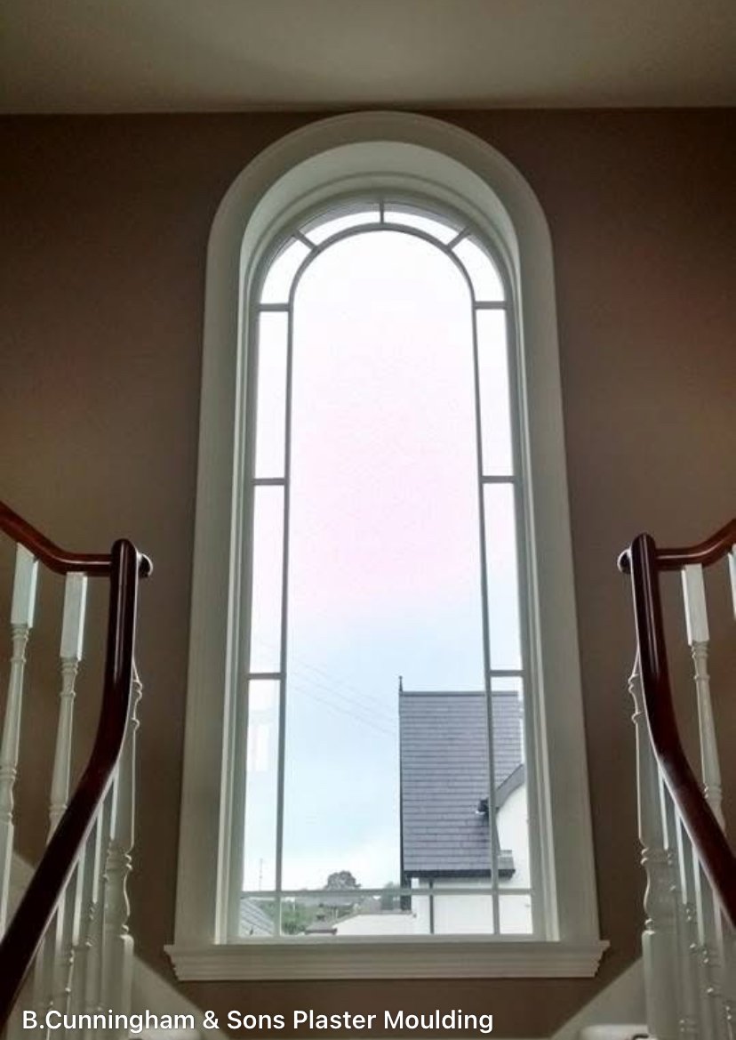 Interior view of a tall arched window with decorative framing, seen from inside a house with staircase handrails on either side.