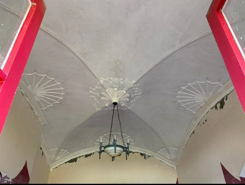 View of a ceiling with decorative moldings and a chandelier in a room under renovation.
