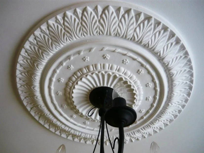 Close-up of an ornate white ceiling medallion with a black ceiling fan attached.