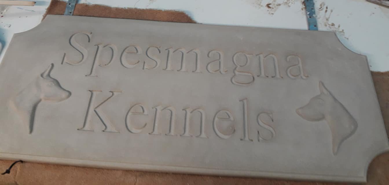 A carved stone sign with the words "Spesnagna Kennels" and dog profiles on either side, placed on a work surface.